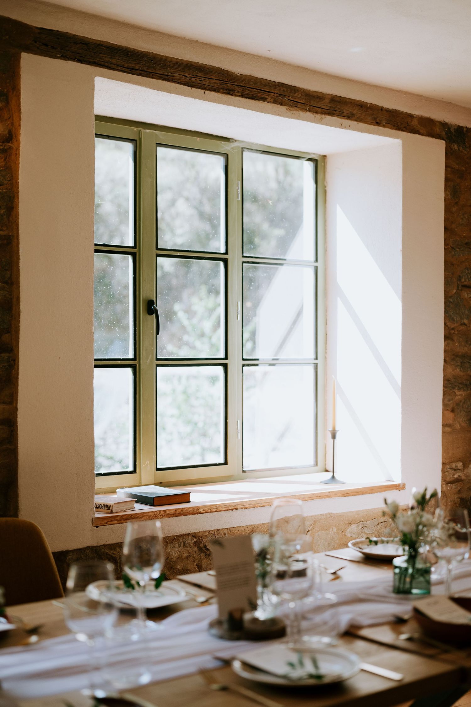 Sunlit window in stone-walled dining room with elegant table settings.