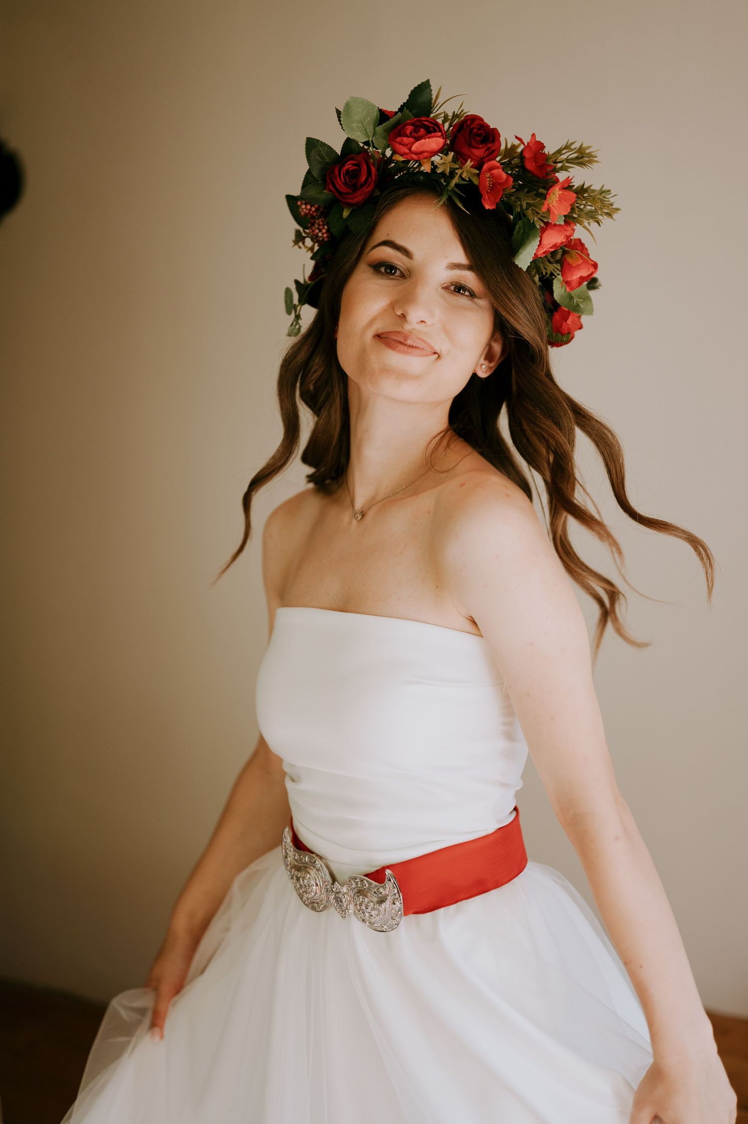 Joyful bridal portrait featuring white ballgown with red accents and floral headpiece.