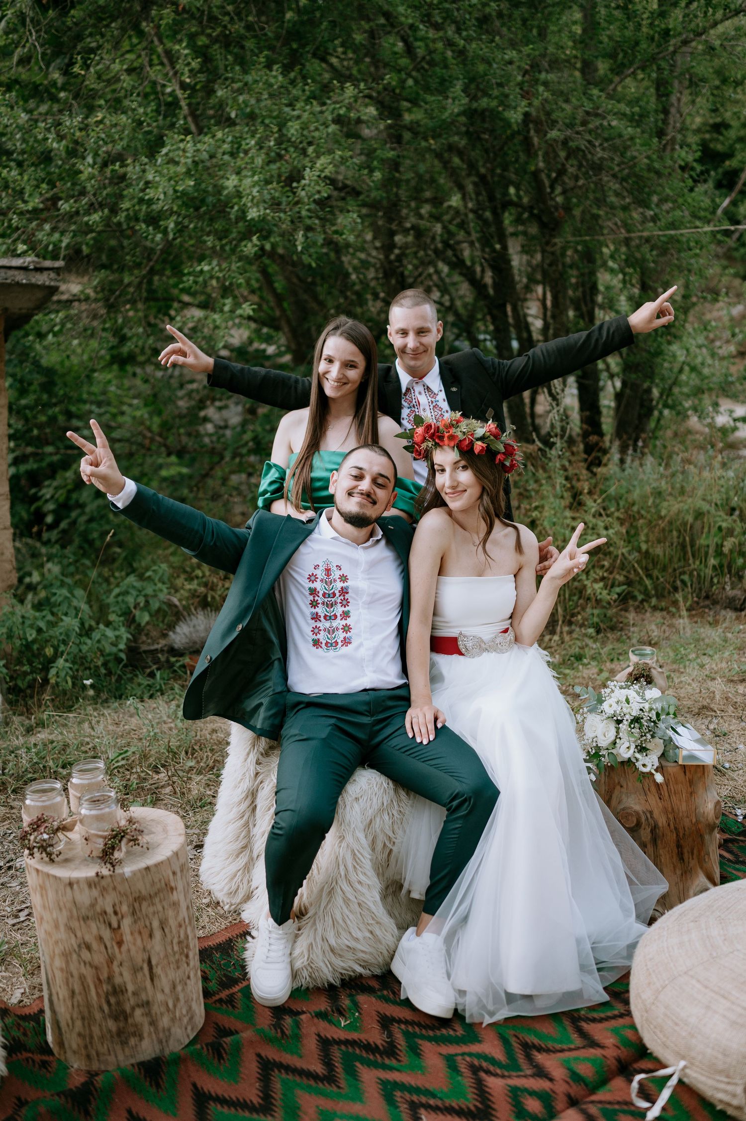 Wedding party posing playfully on rustic outdoor setting with wooden stumps and bohemian decor.
