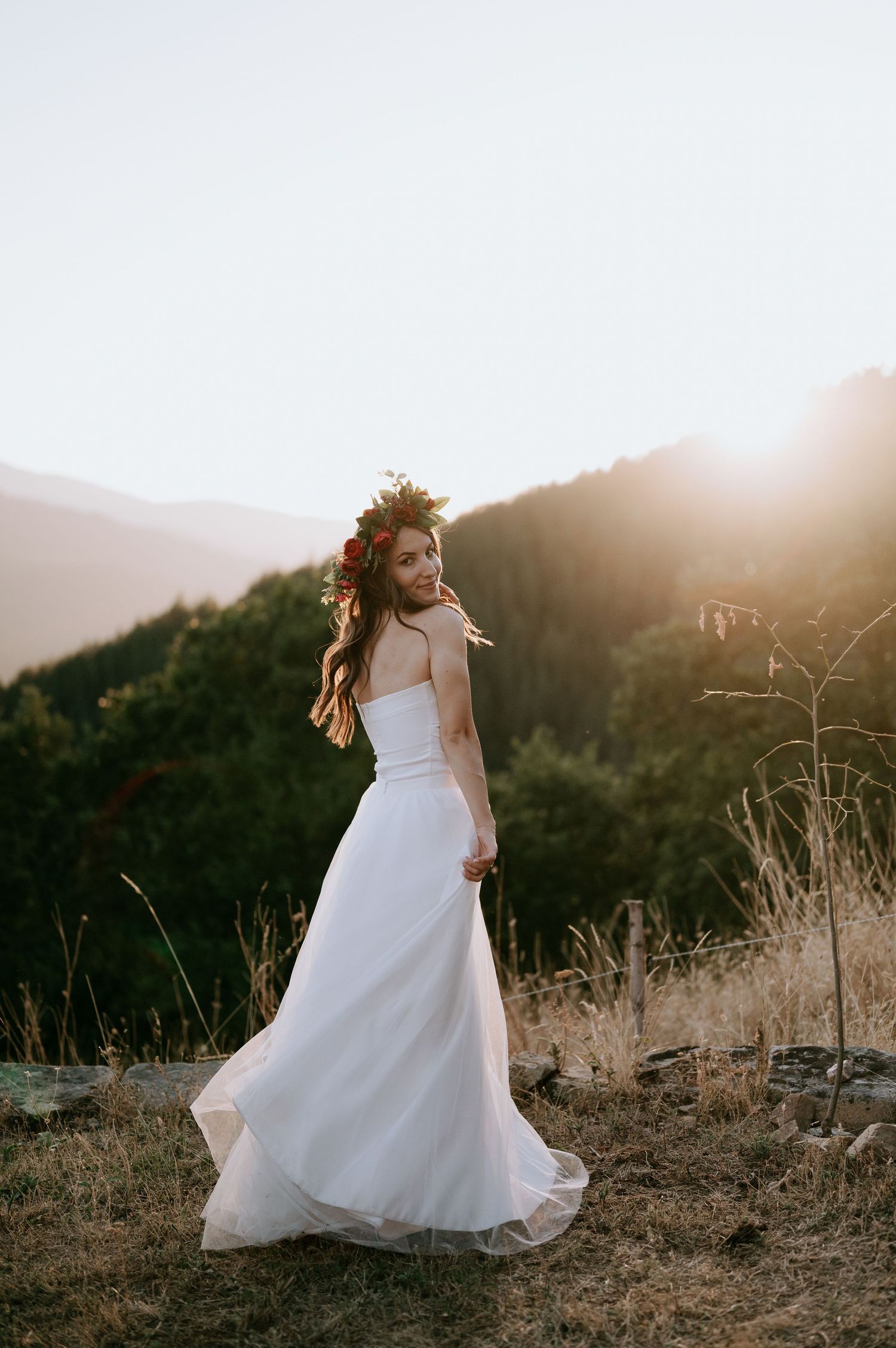 A white wedding gown twirls gracefully against a mountainous backdrop at sunset.