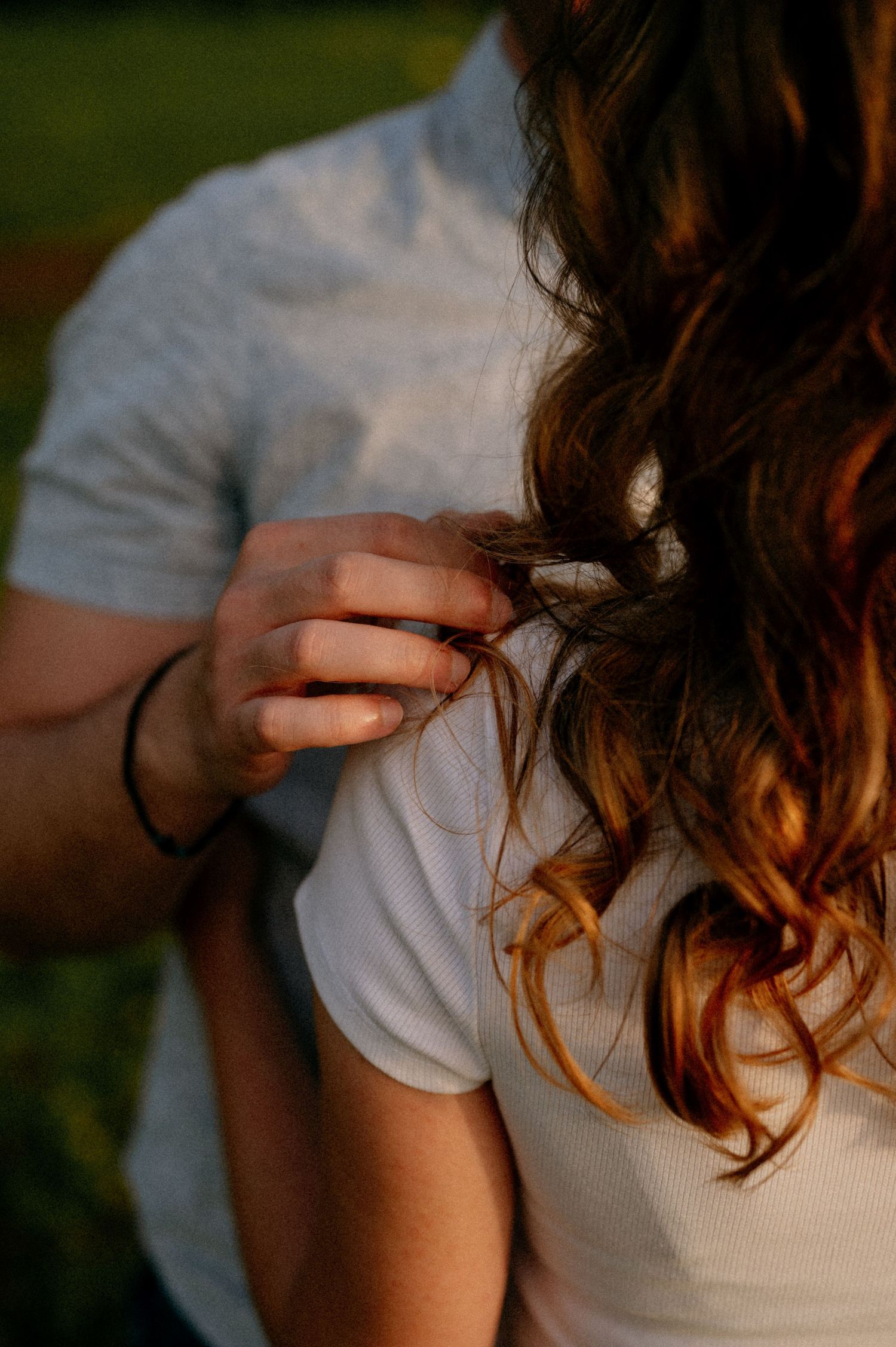 Soft focus image of hands running through illuminated brown wavy hair.