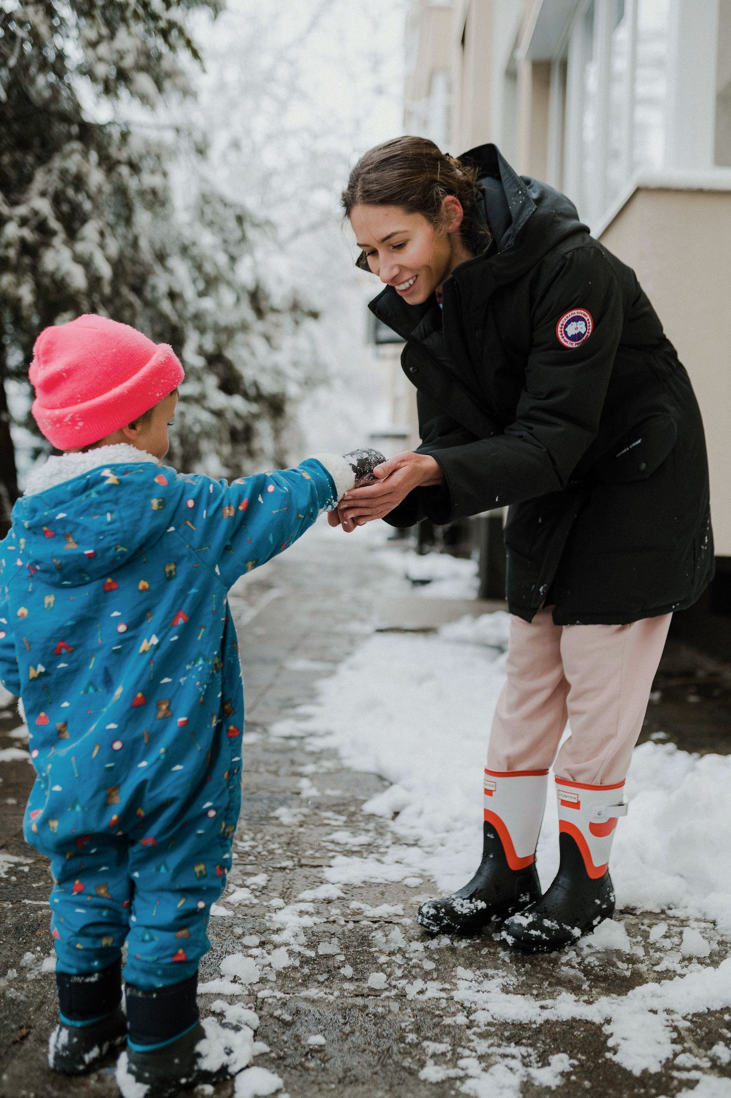 A parent and child in winter clothing play together in the snow on a snowy winter day.