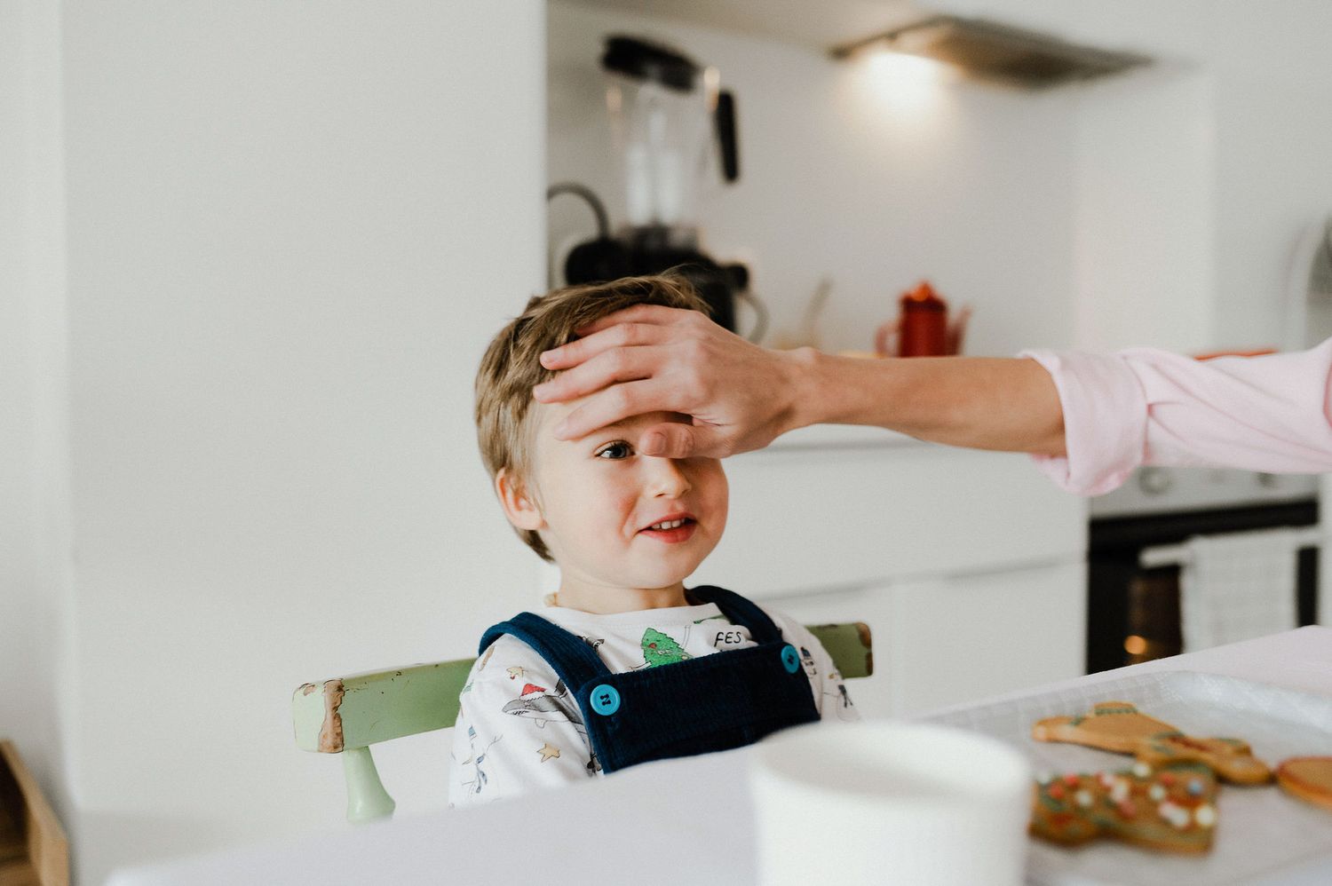 Baby smiling while being fed with a spoon in a bright white kitchen.