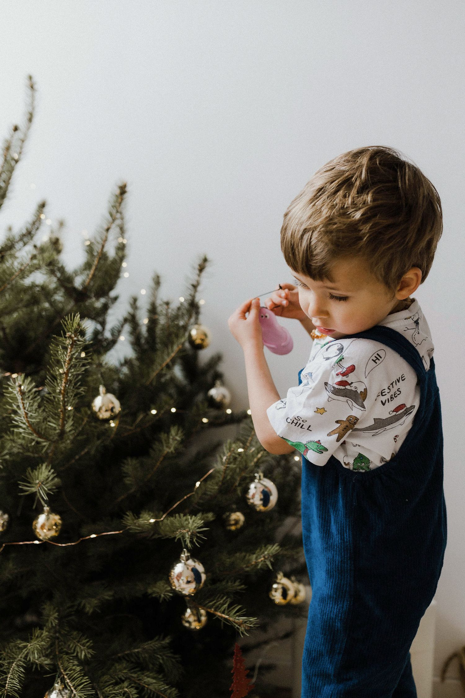 Young child in blue sweater decorating a Christmas tree with silver ornaments.