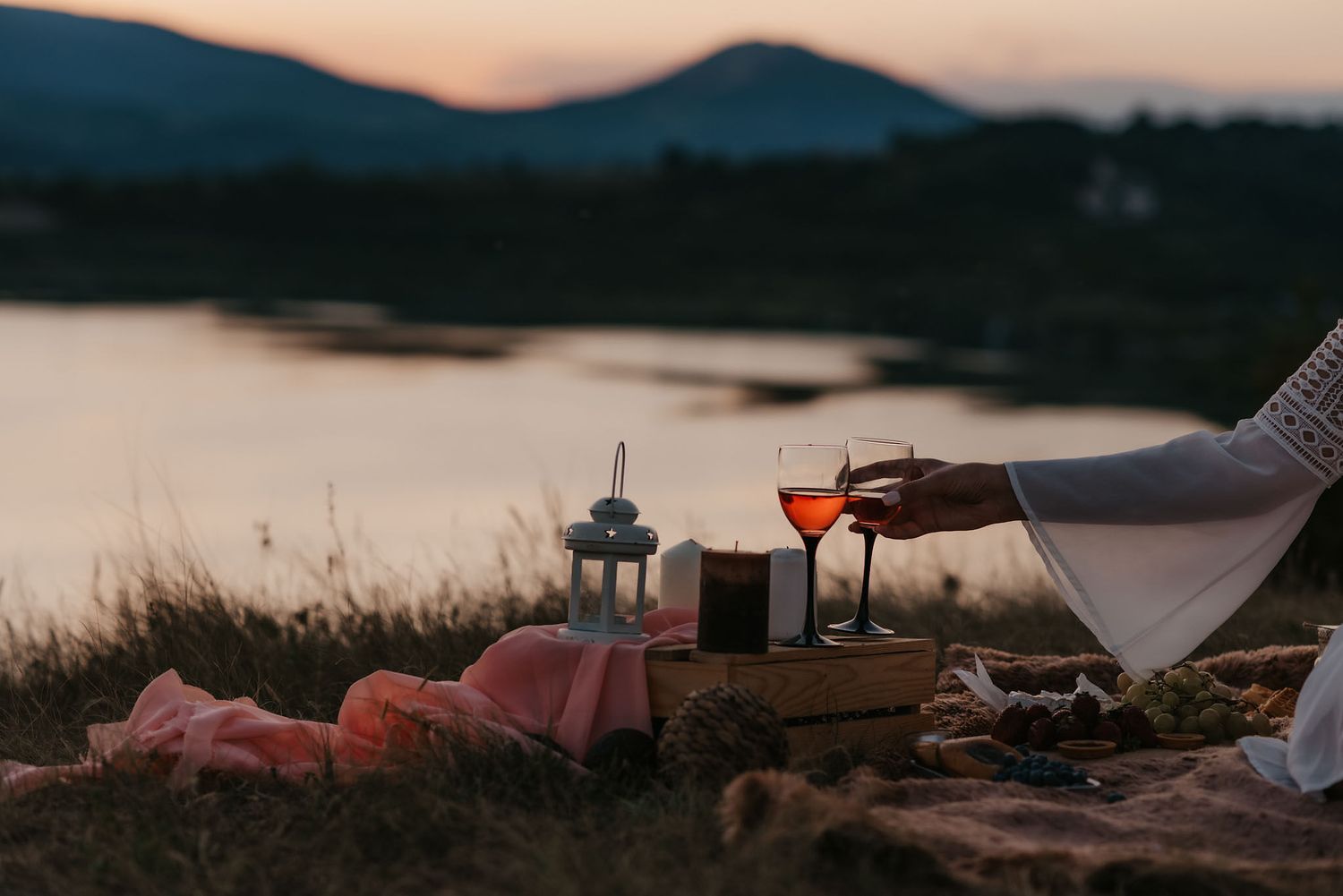 Cozy picnic spread laid out by a lake during sunset with mountains in the background.