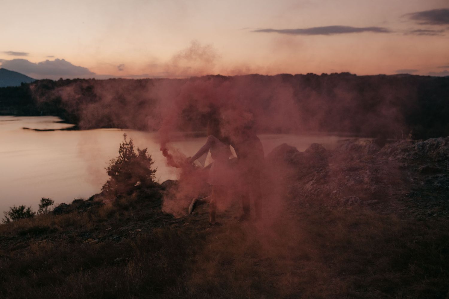 Panoramic sunset view of a lake with red smoke effects in the foreground.