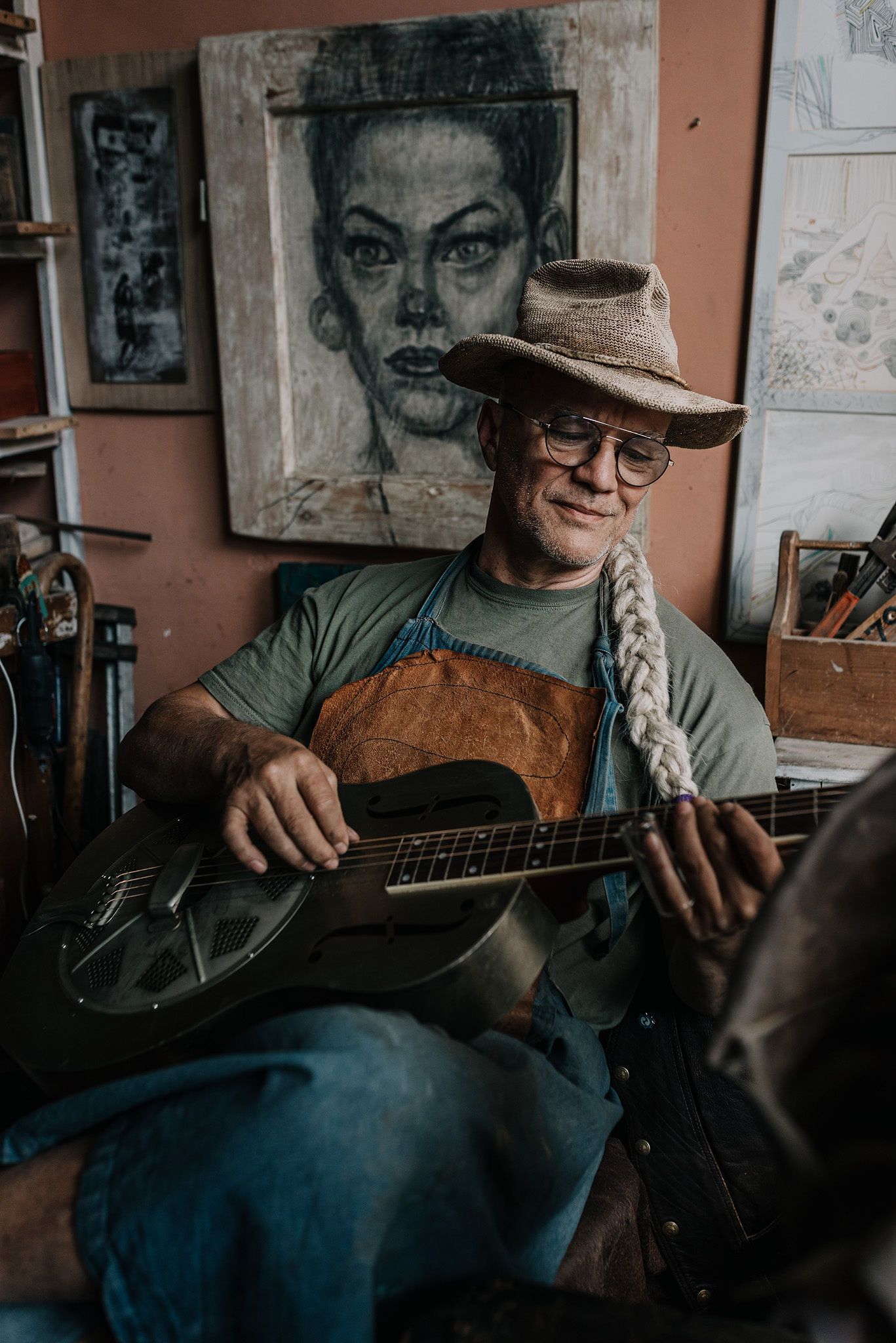 Musician playing acoustic guitar in front of wall decorated with artwork.