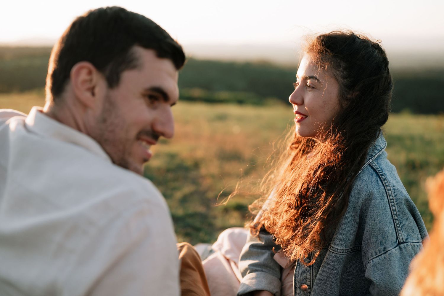 Couple embraces in golden sunlight while sitting together in a grassy meadow at sunset.