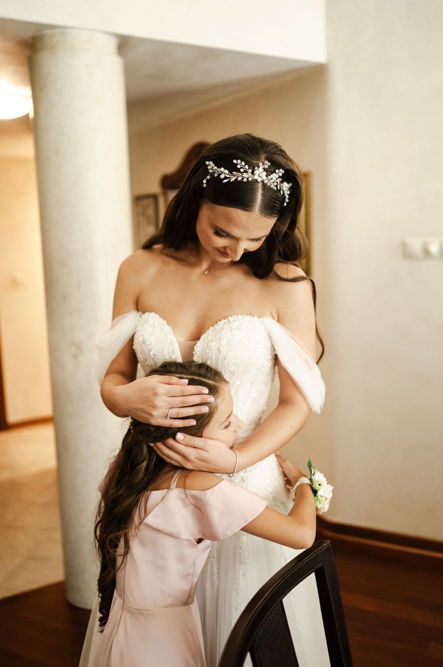 Two people share a tender moment in formal attire near white columns.