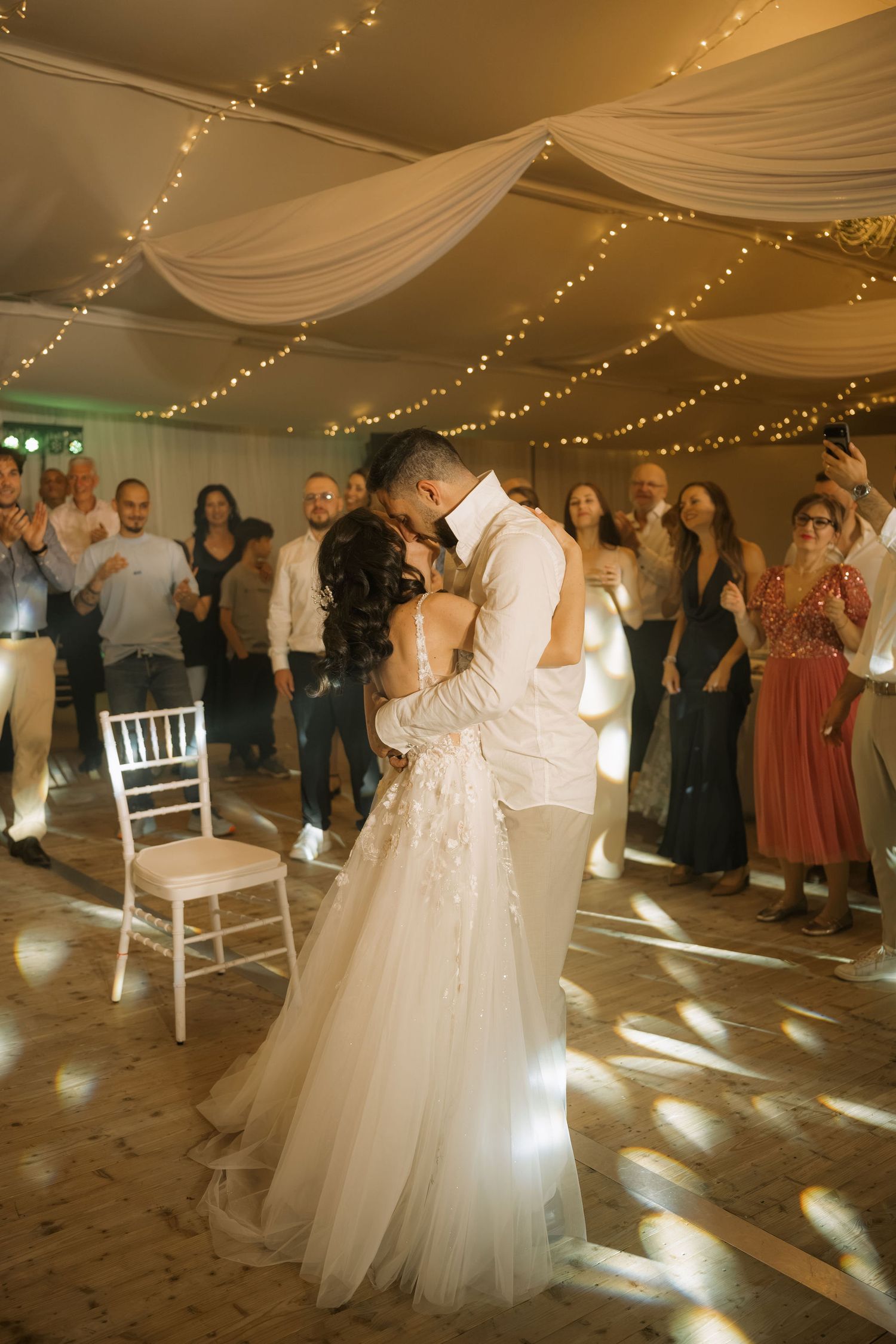 Bride and groom share first dance under fairy lights and draped ceiling at elegant wedding reception.