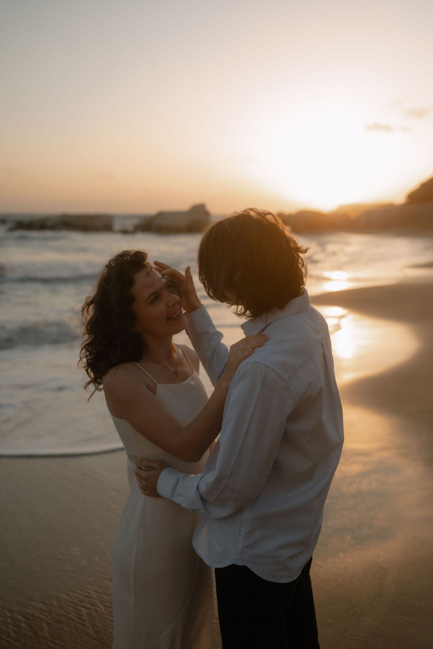 Couple embracing romantically on a sandy beach at golden sunset with ocean waves in the background.
