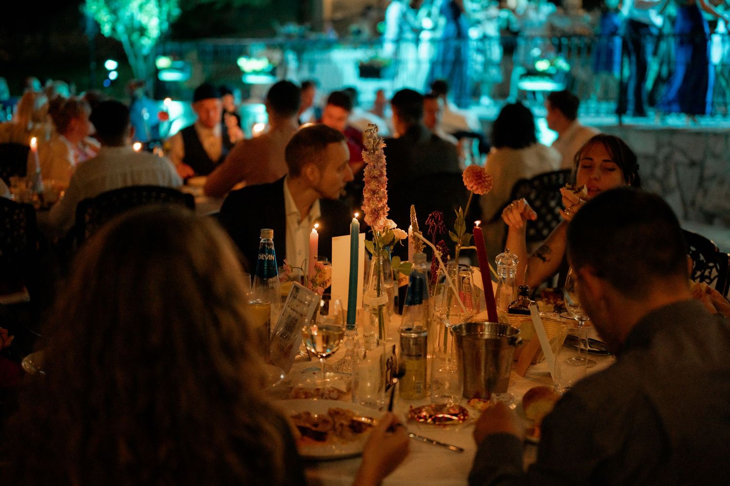 Candlelit tables at a dimly lit wedding reception with guests enjoying dinner and conversation in a rustic setting.