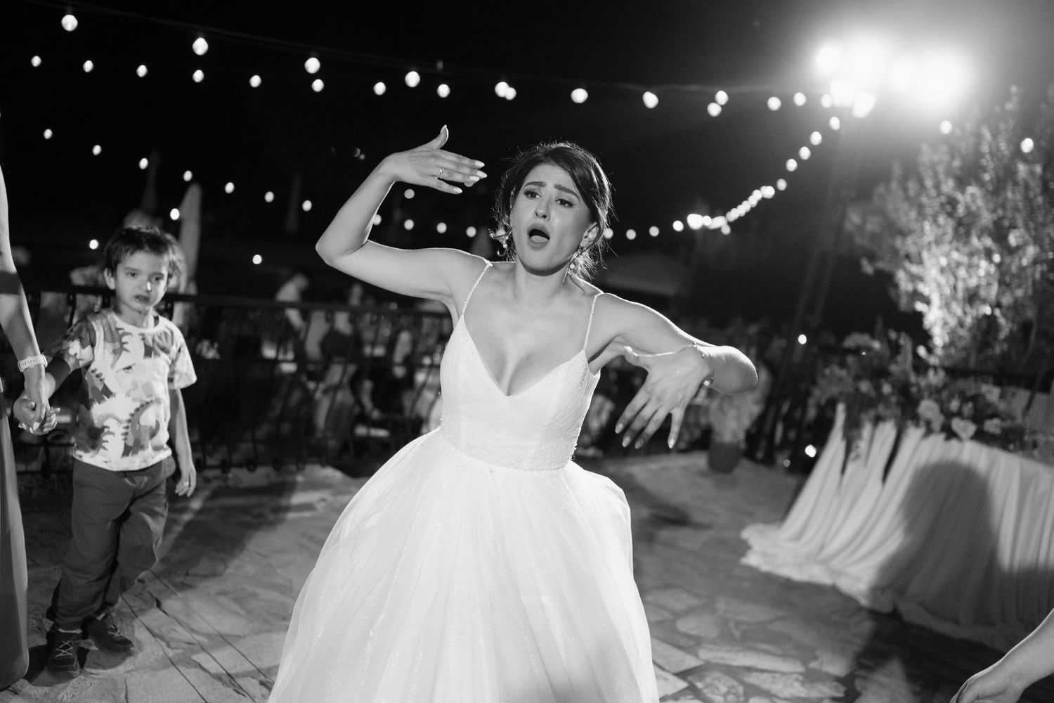 A couple shares their first dance at an outdoor wedding reception under string lights at night.