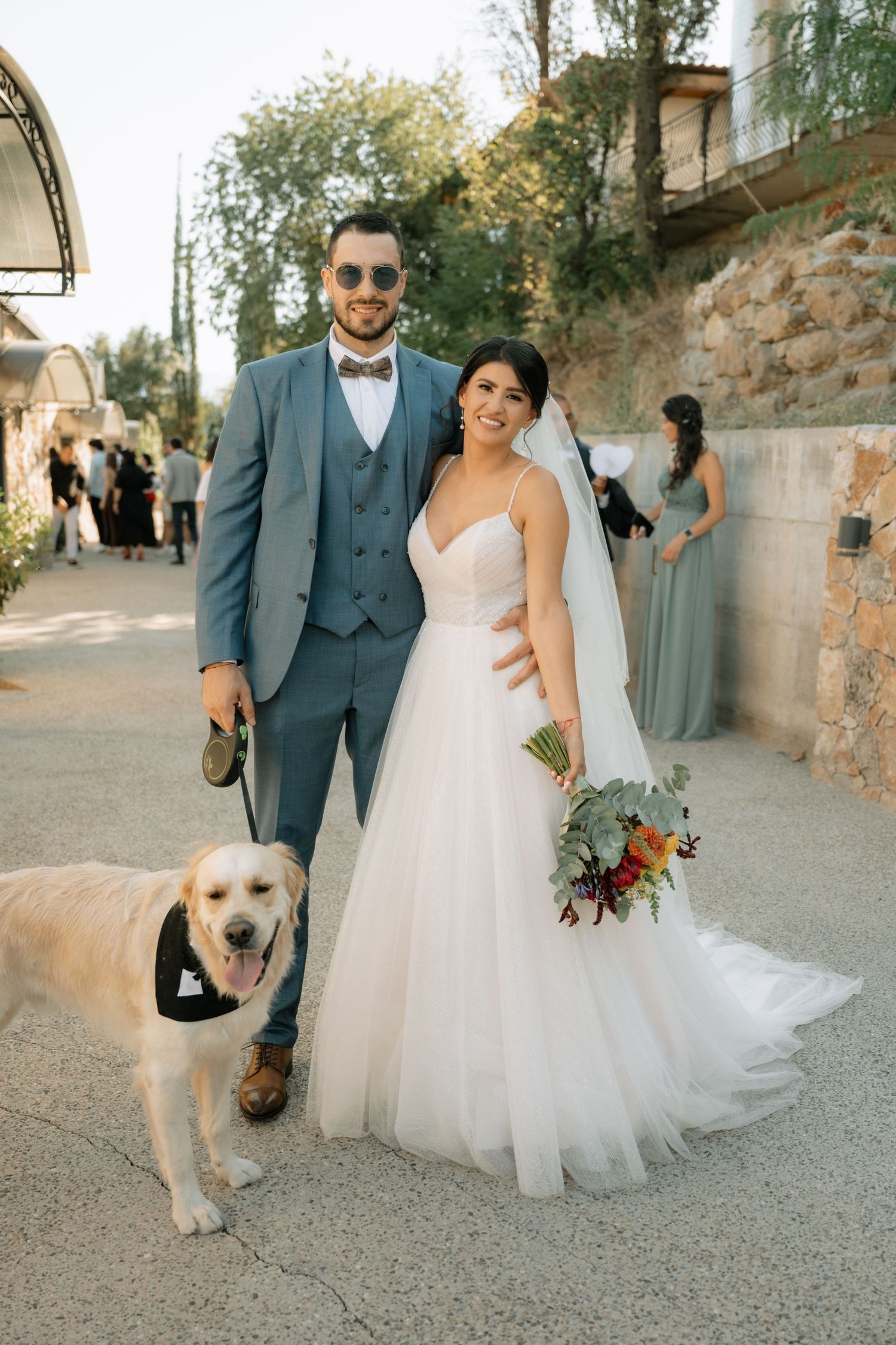 A wedding couple poses with their golden retriever on a stone pathway during their special day.