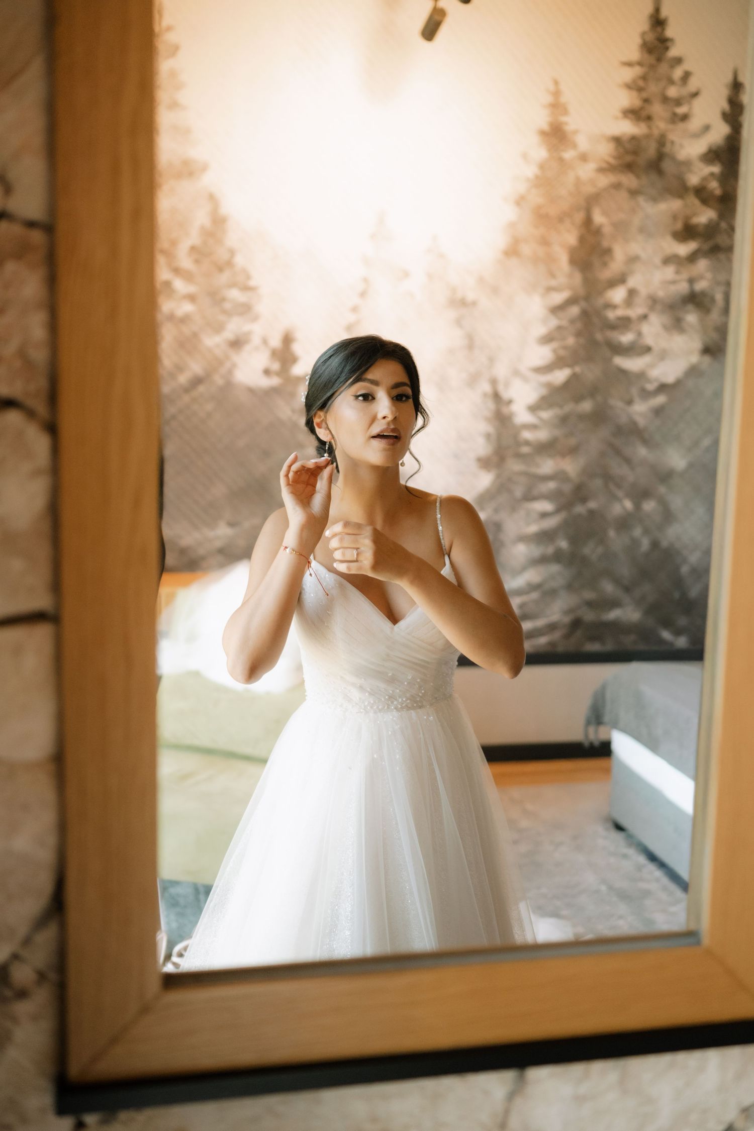 Three mirror reflections show a bride in a white dress getting ready against a nature-themed wall mural.