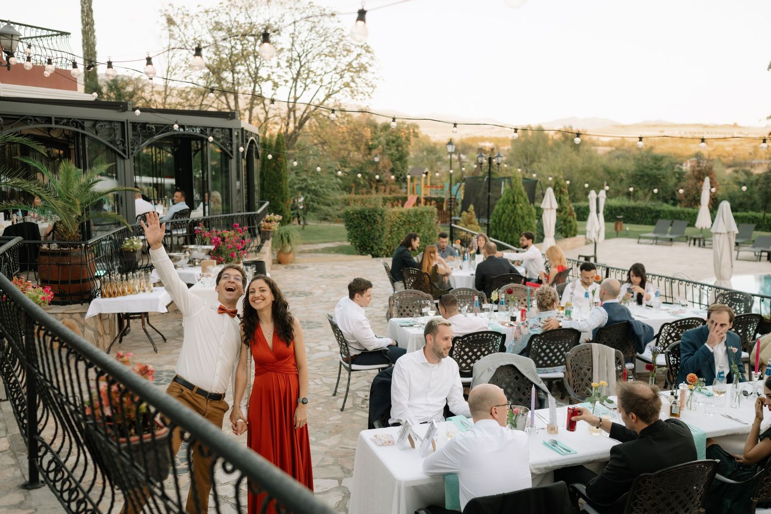Outdoor wedding reception setup with white tablecloths and chairs arranged on a patio during golden hour.