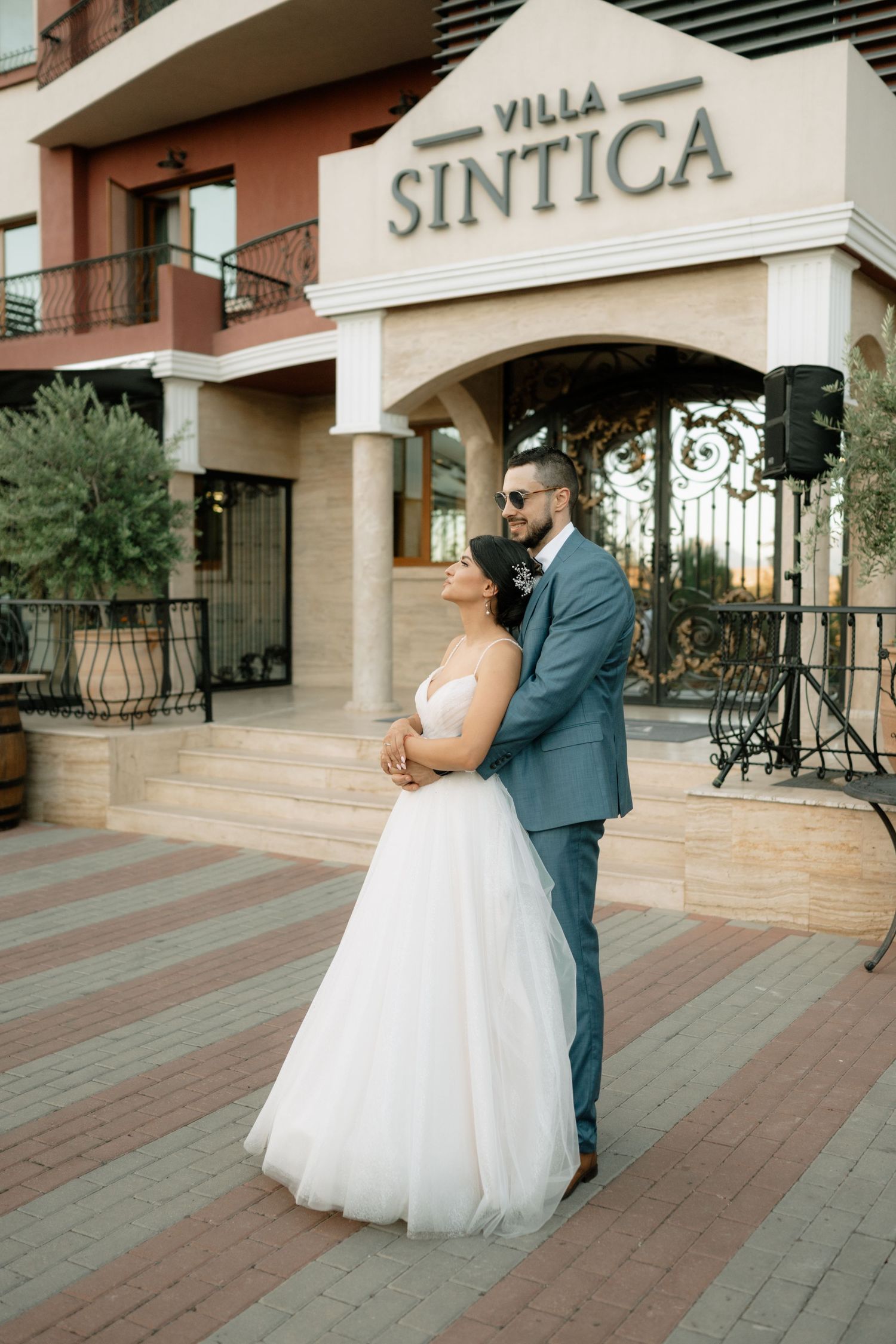 A couple in wedding attire shares an intimate dance moment on a tiled terrace outside a villa entrance.