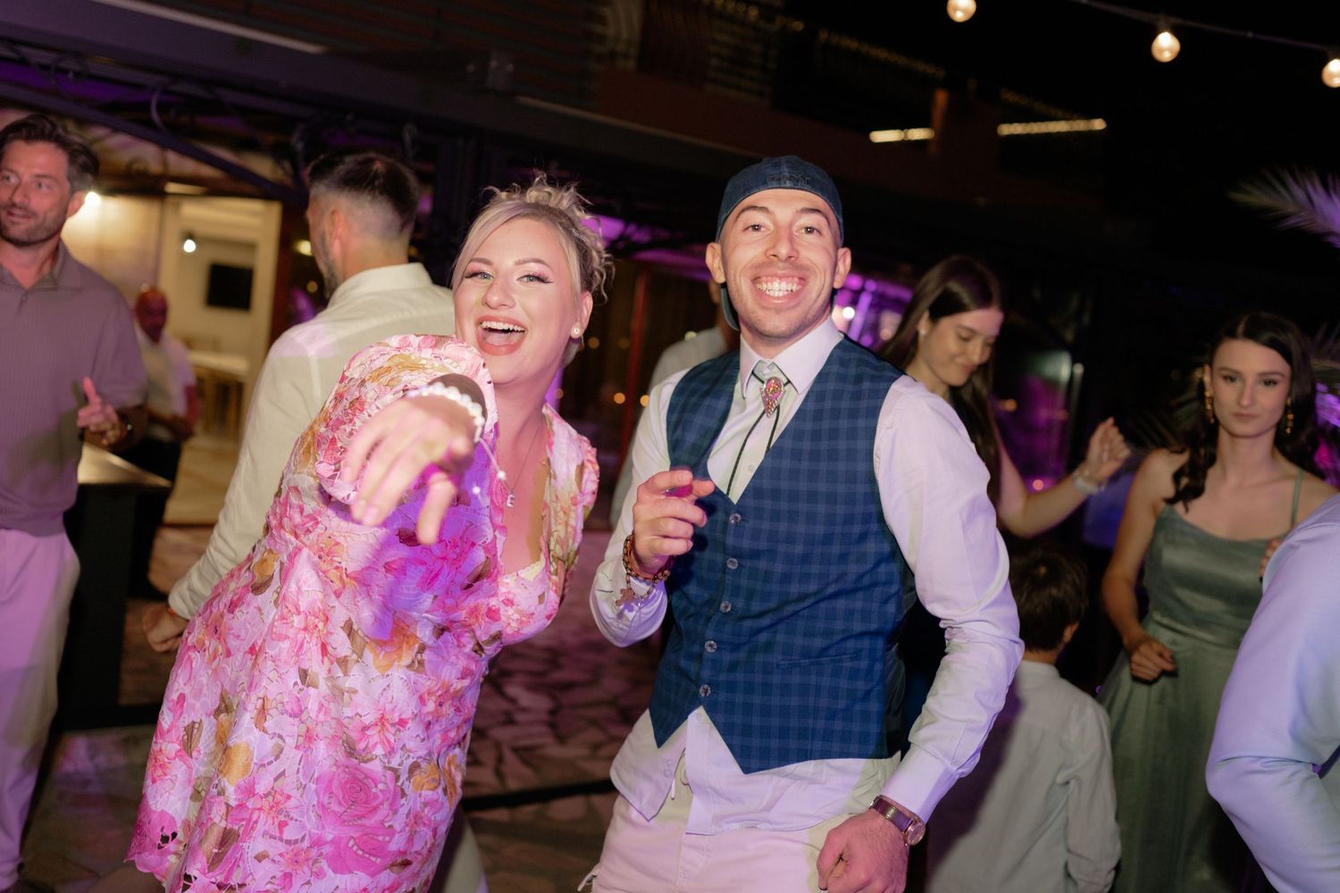 People dancing and celebrating at a lively wedding reception with colorful lighting and festive atmosphere.