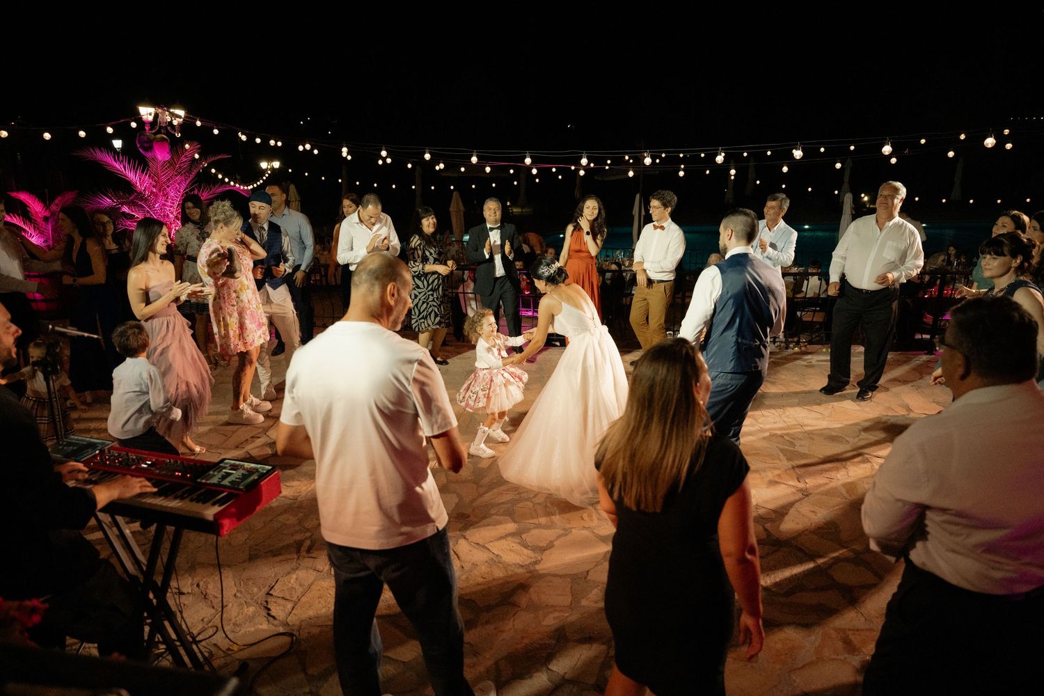 People dancing and celebrating at a nighttime outdoor wedding reception under string lights.