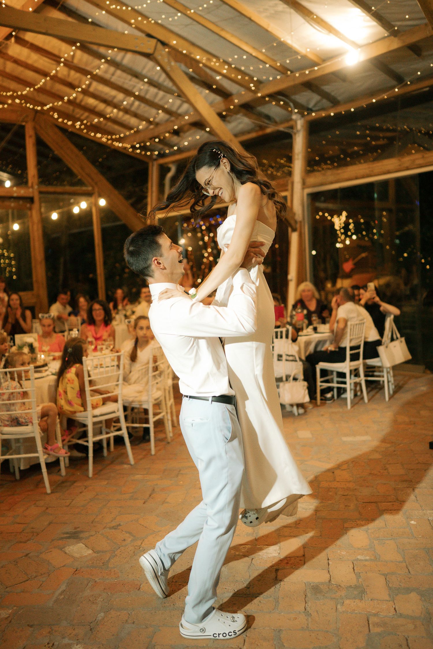 A couple dances together at a rustic barn wedding reception decorated with twinkling lights overhead.
