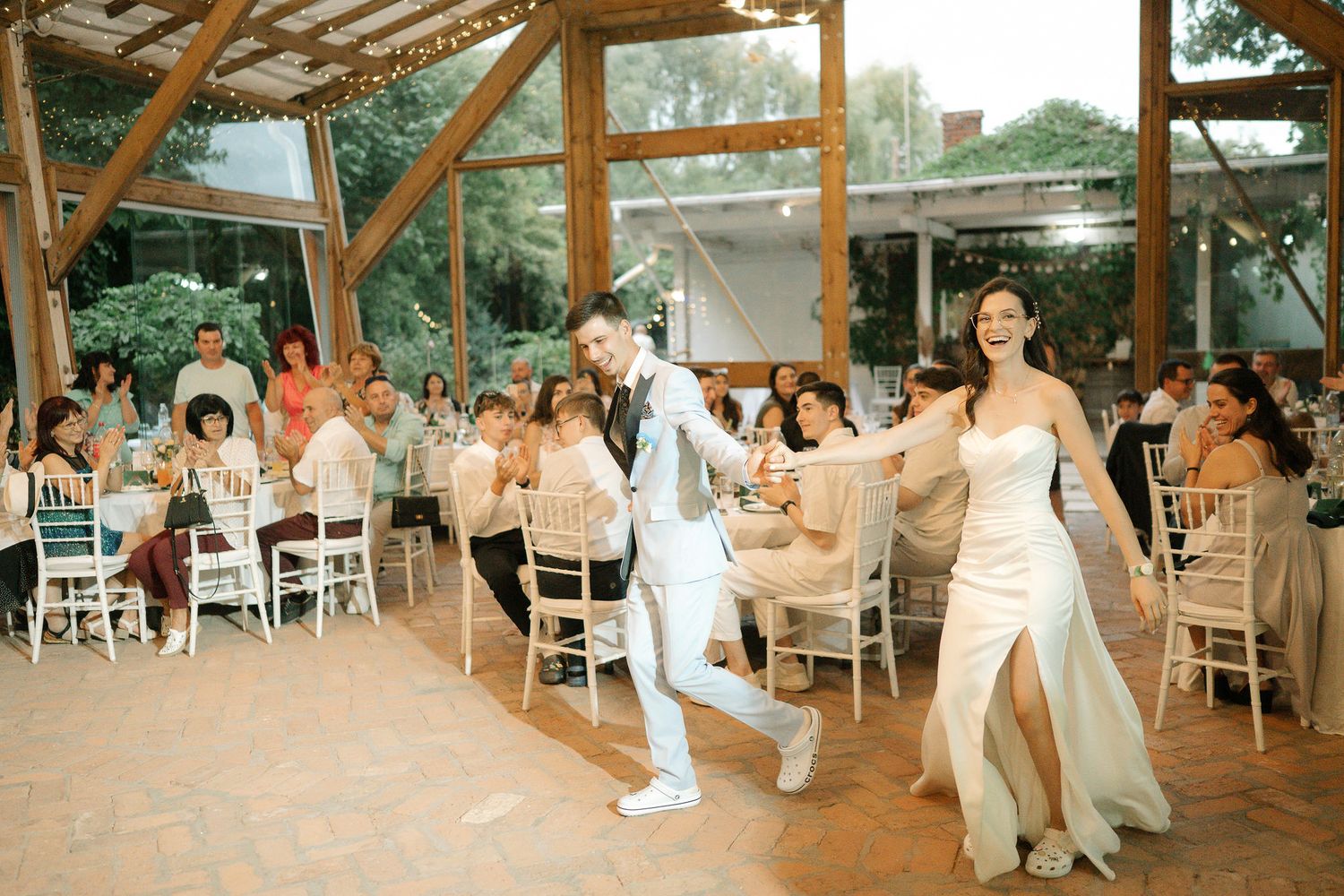 Wedding guests dance and celebrate together on a rustic wooden dance floor under string lights at an outdoor reception.
