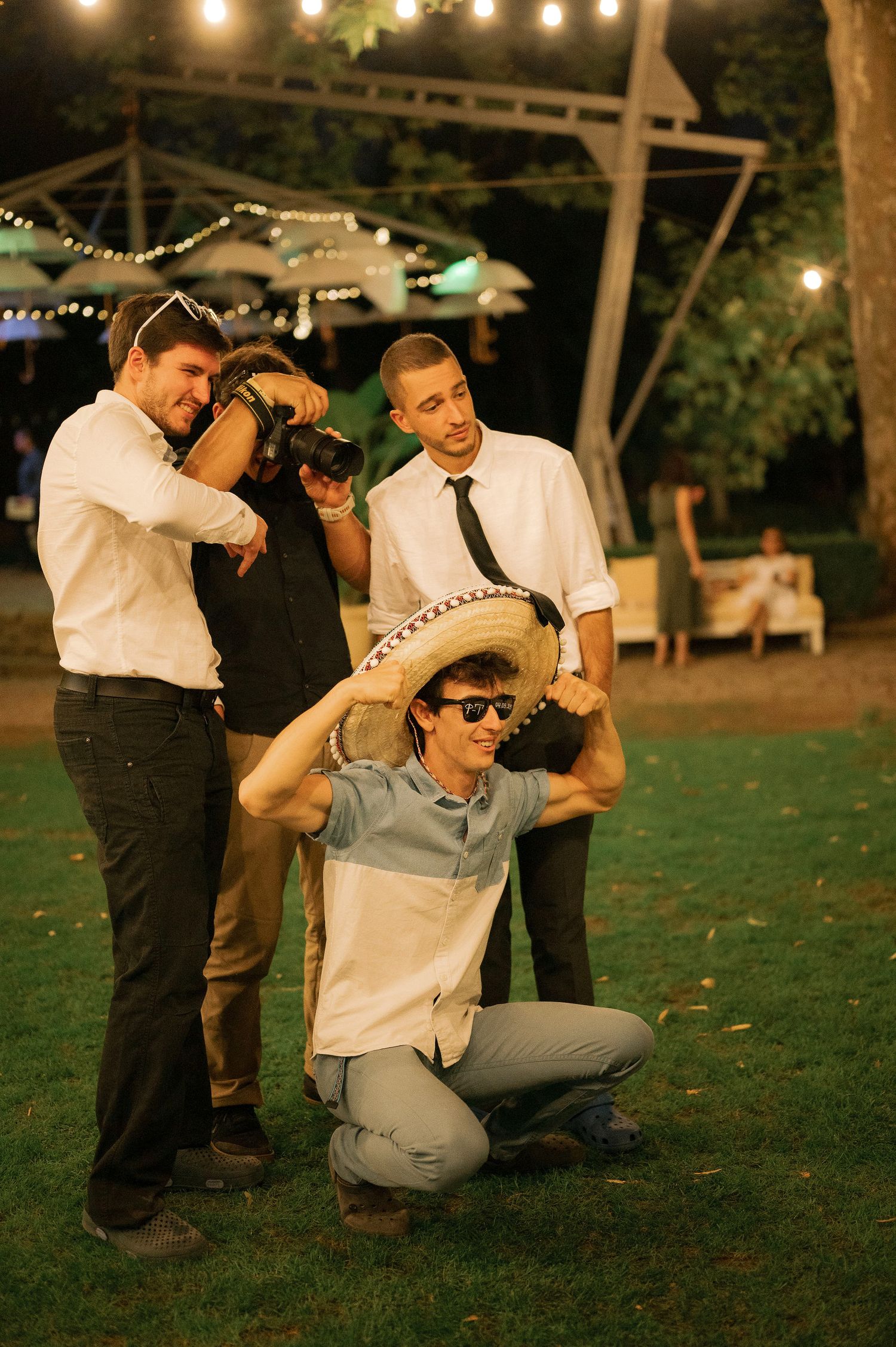 A group dances together outdoors at night under string lights in a casual party setting.