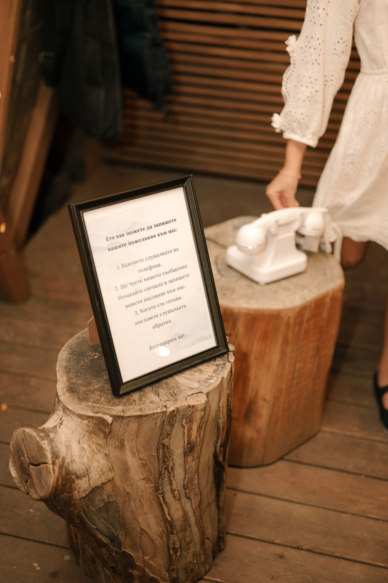 A framed text sign sits on rustic wood stumps with someone in a white dress standing nearby.