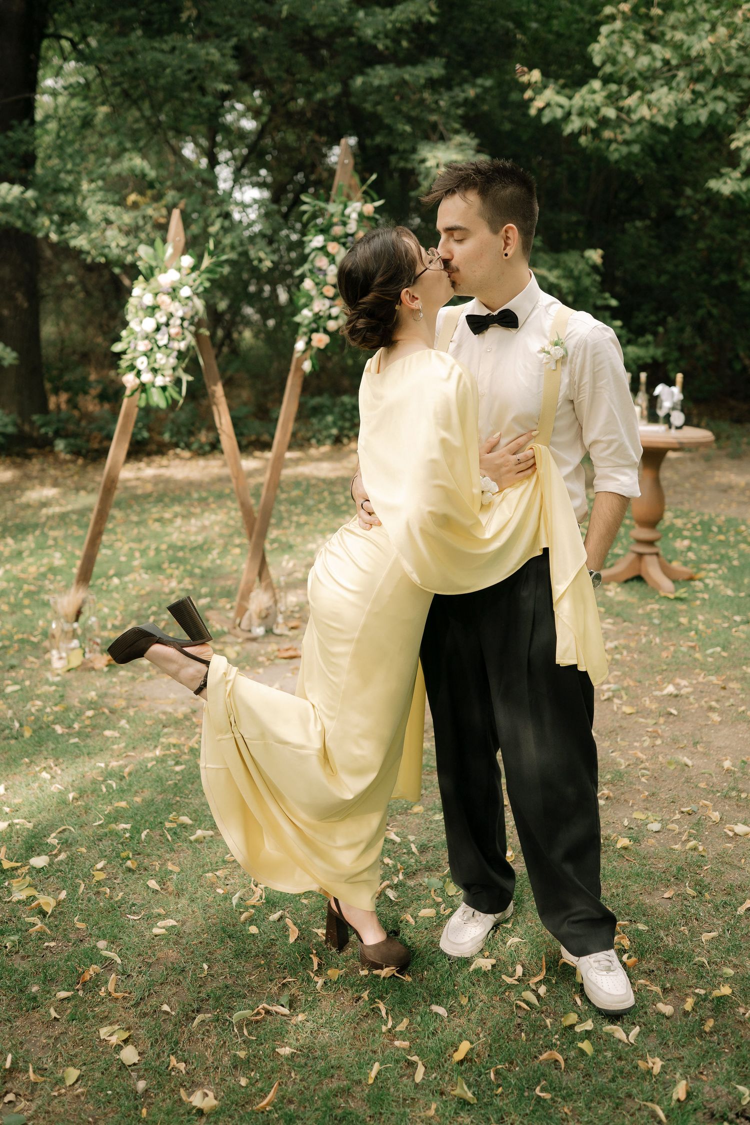 A couple in formal attire performs a romantic dip dance move on grass covered with fallen autumn leaves.