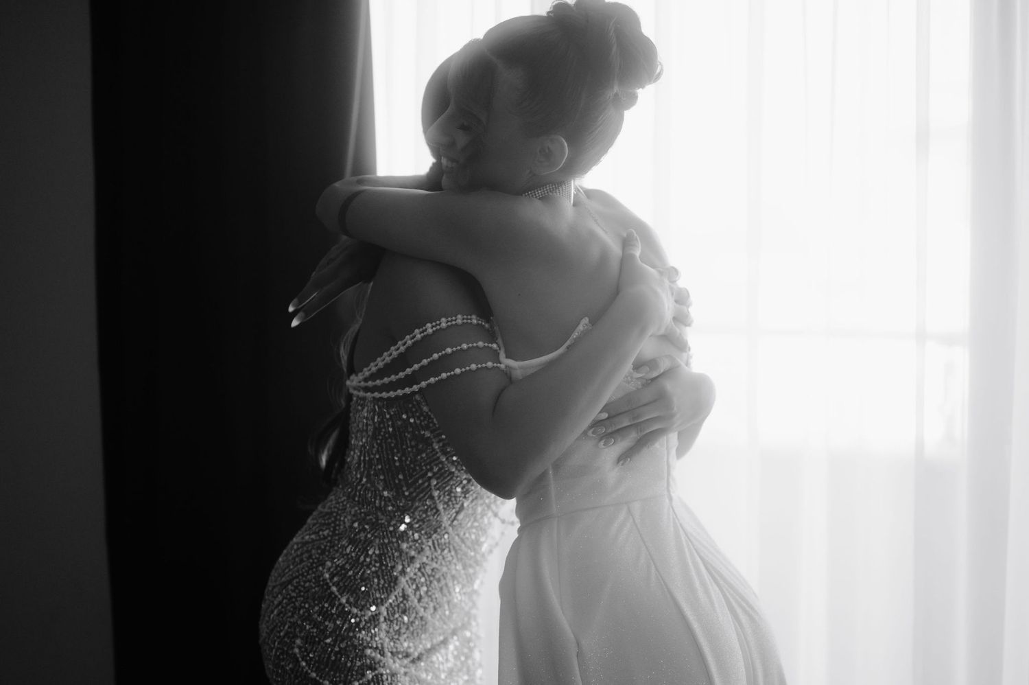 A silhouetted bride in a wedding dress stands in front of a bright window creating a dramatic backlit effect.