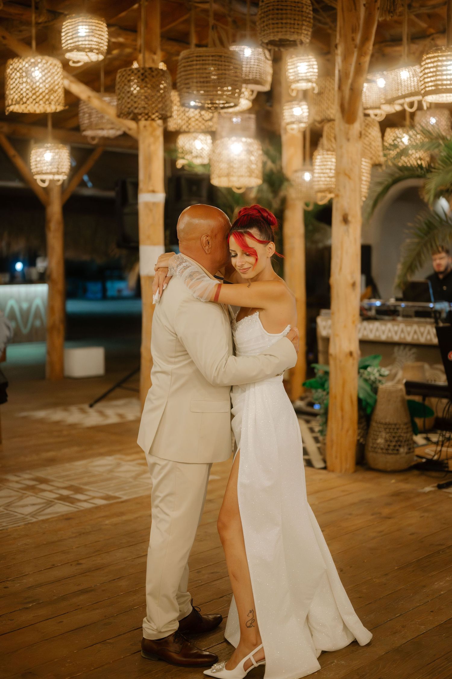 A couple shares a romantic dance moment under crystal chandeliers in a rustic wooden venue during their wedding reception.