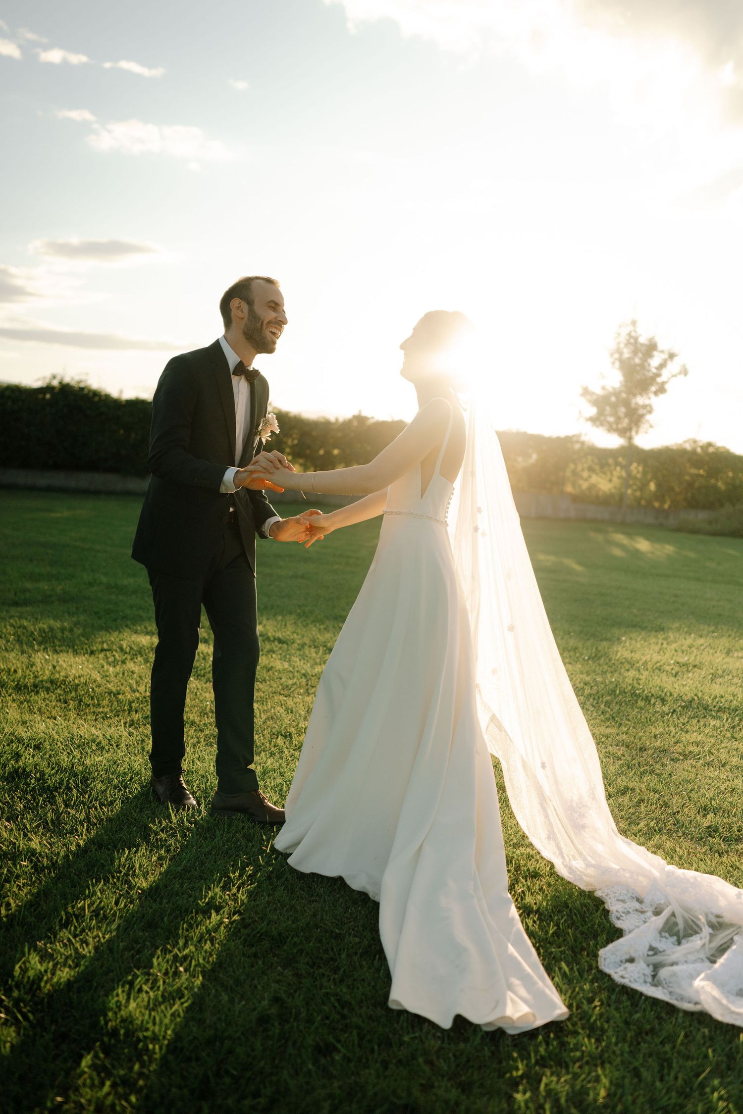 A couple shares a romantic moment at sunset in an outdoor wedding setting with a flowing white veil and dress.