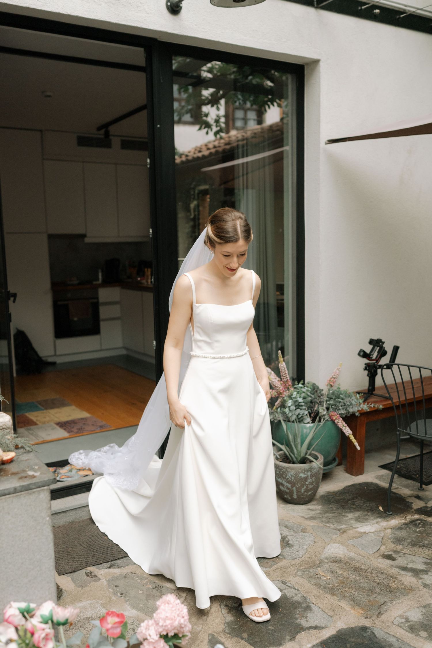 Series of photos showing a bride in a simple white dress walking on a stone patio with potted plants.