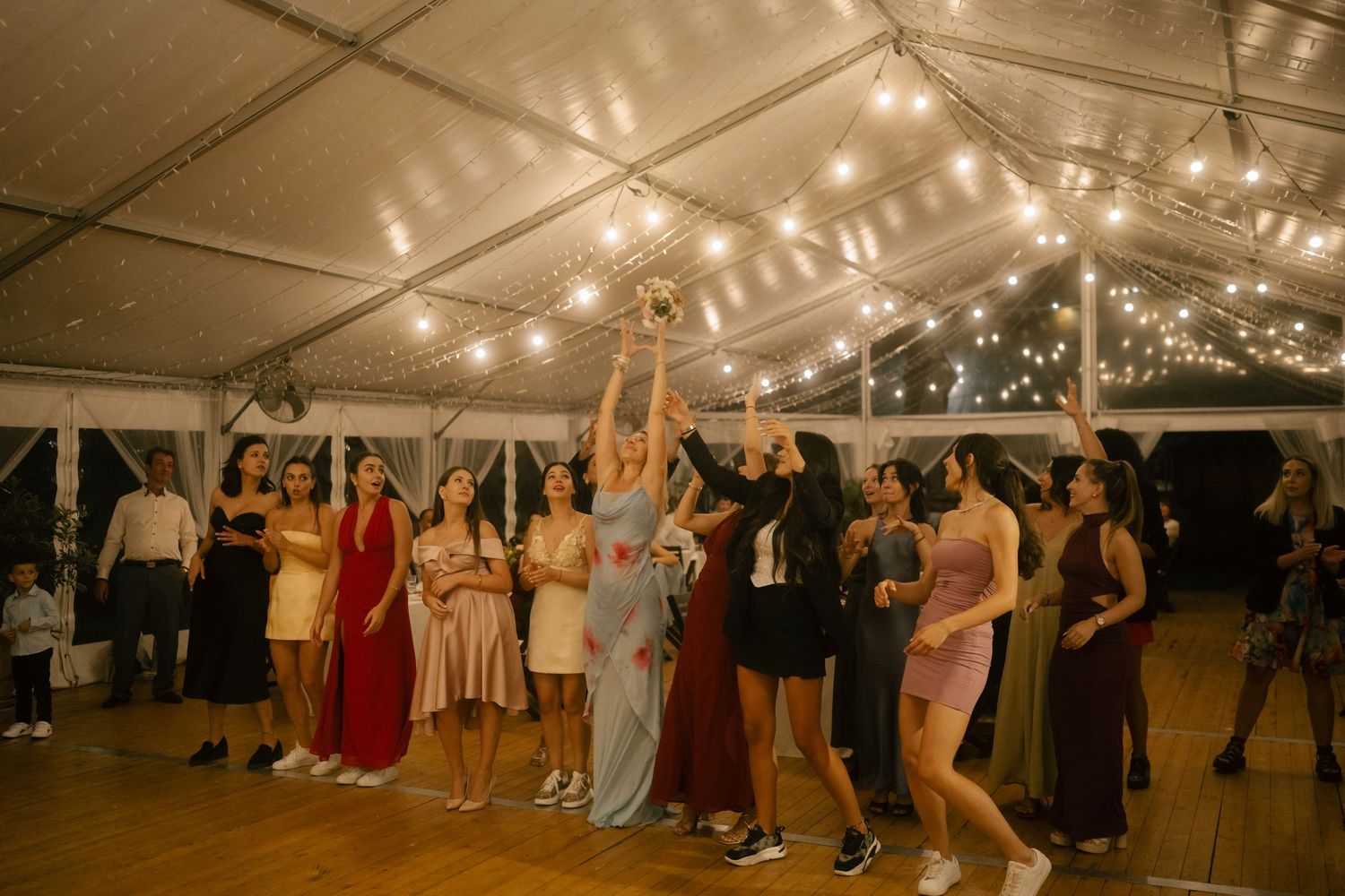 Wedding reception tent filled with guests dancing under warm string lights on a wooden deck.