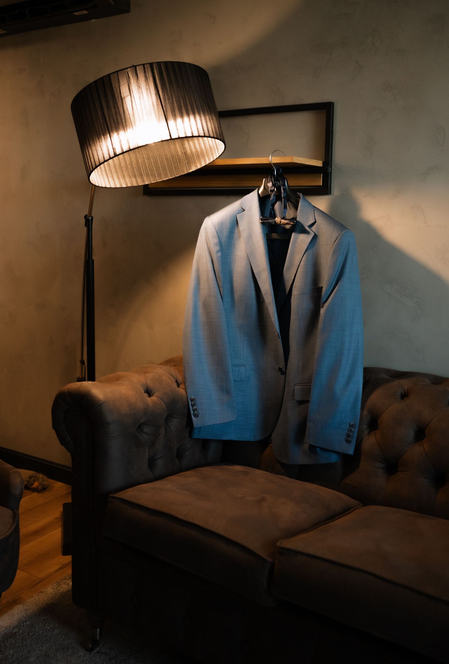 A light blue suit jacket hangs mysteriously in a dimly lit room with dramatic lamp lighting casting moody shadows.