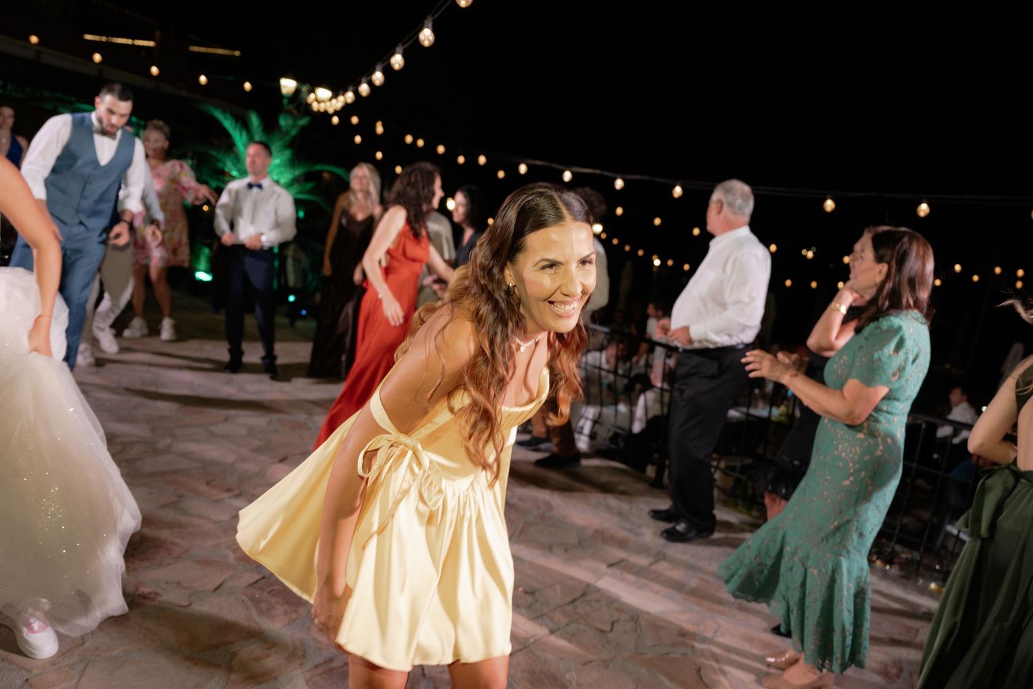People dancing and celebrating at an outdoor evening reception with string lights overhead on a wooden deck.