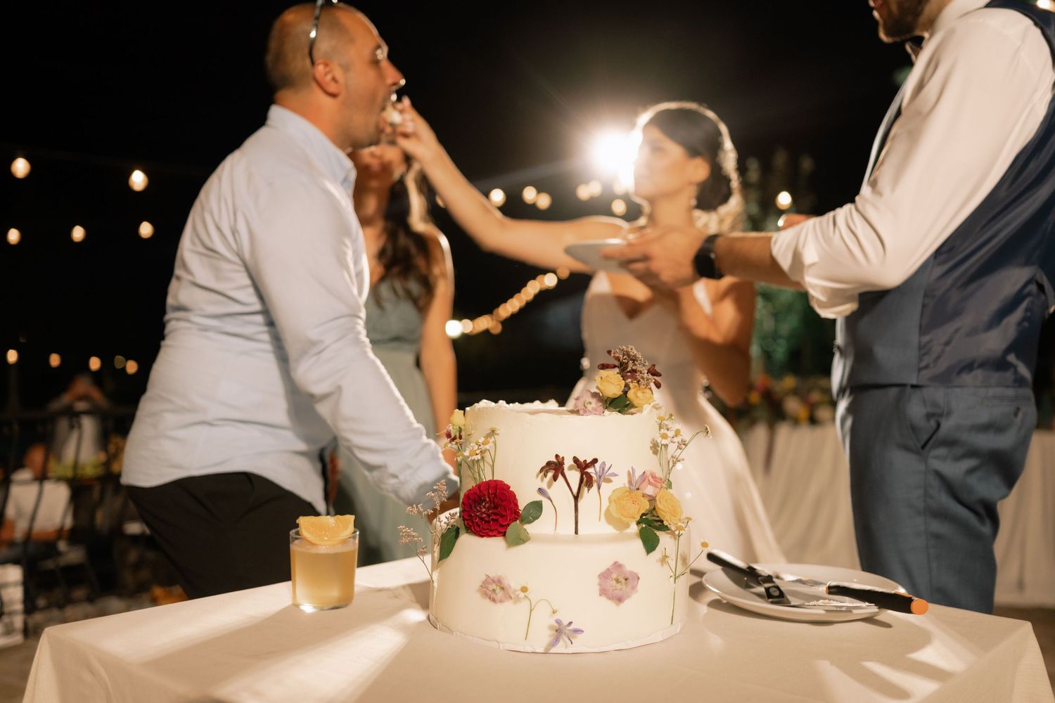 A couple cuts their white wedding cake together during an evening outdoor reception celebration.