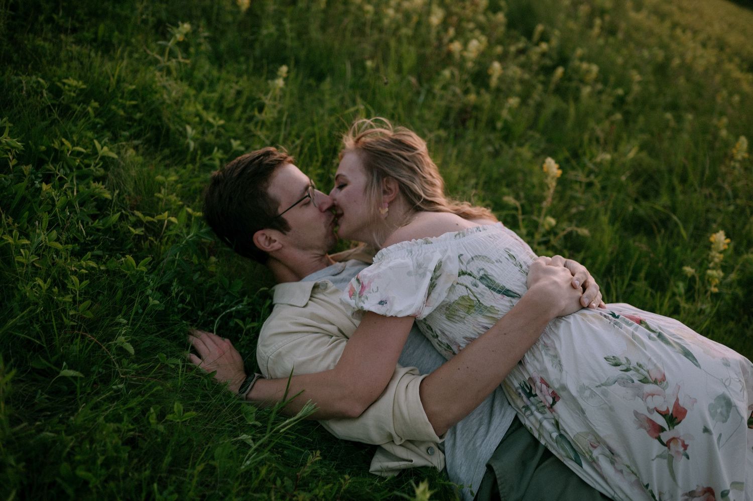 A romantic moment captured in a meadow with two people embracing among wildflowers.