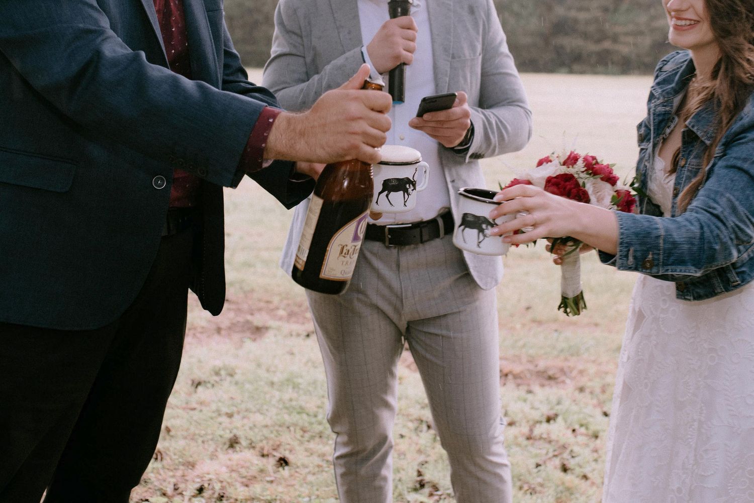 Wedding party members interact during outdoor ceremony under pine trees.
