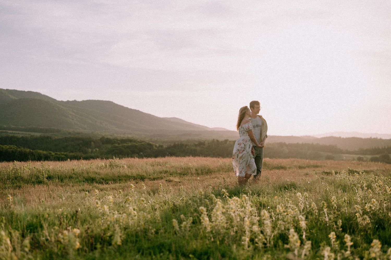 Couple embracing in a scenic mountain meadow during golden hour.