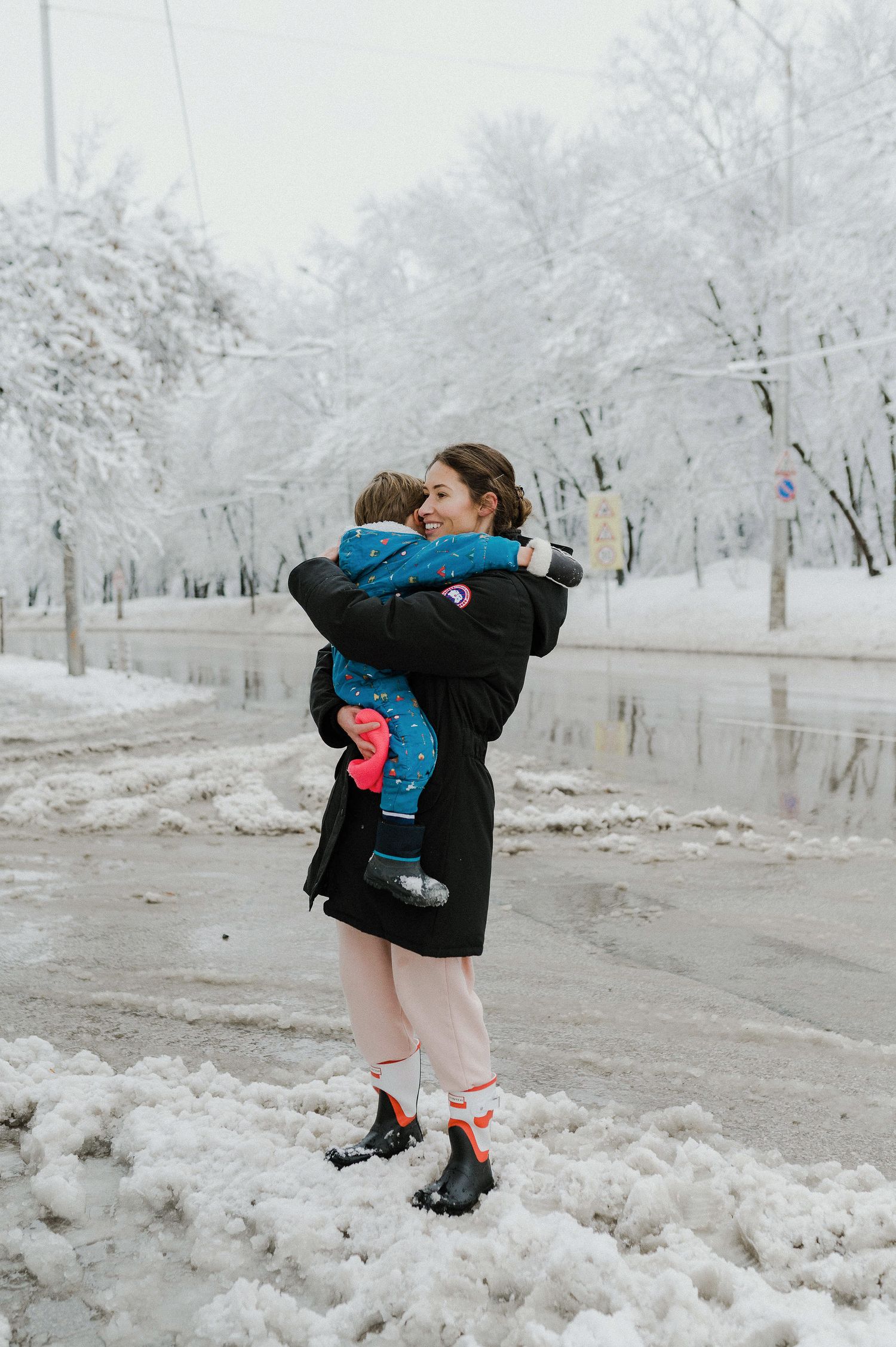 A snowy winter scene in a park with two people embracing on a snow-covered path surrounded by frost-covered trees.