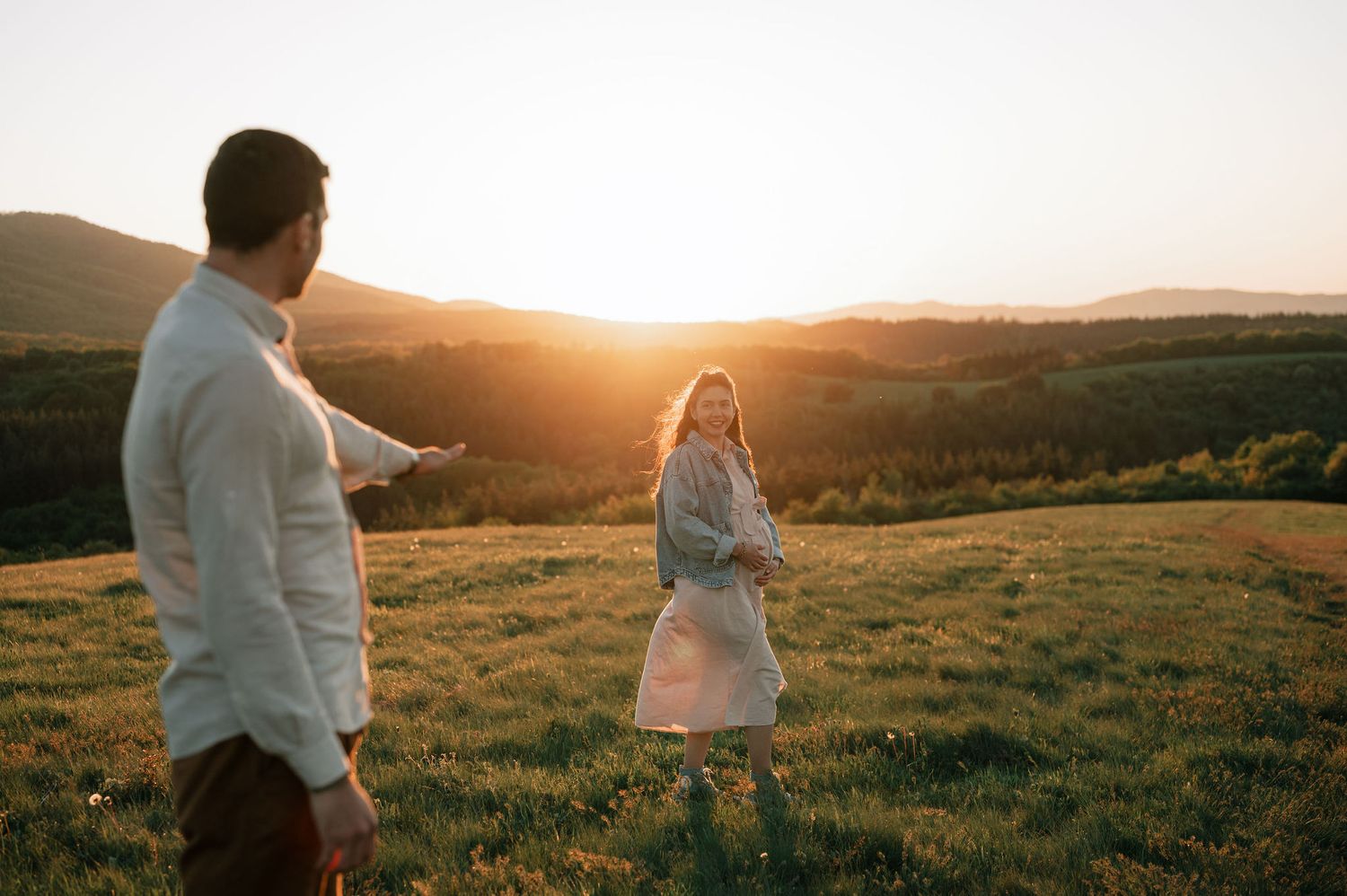 Couple walking together in a golden field at sunset with mountains in the background.