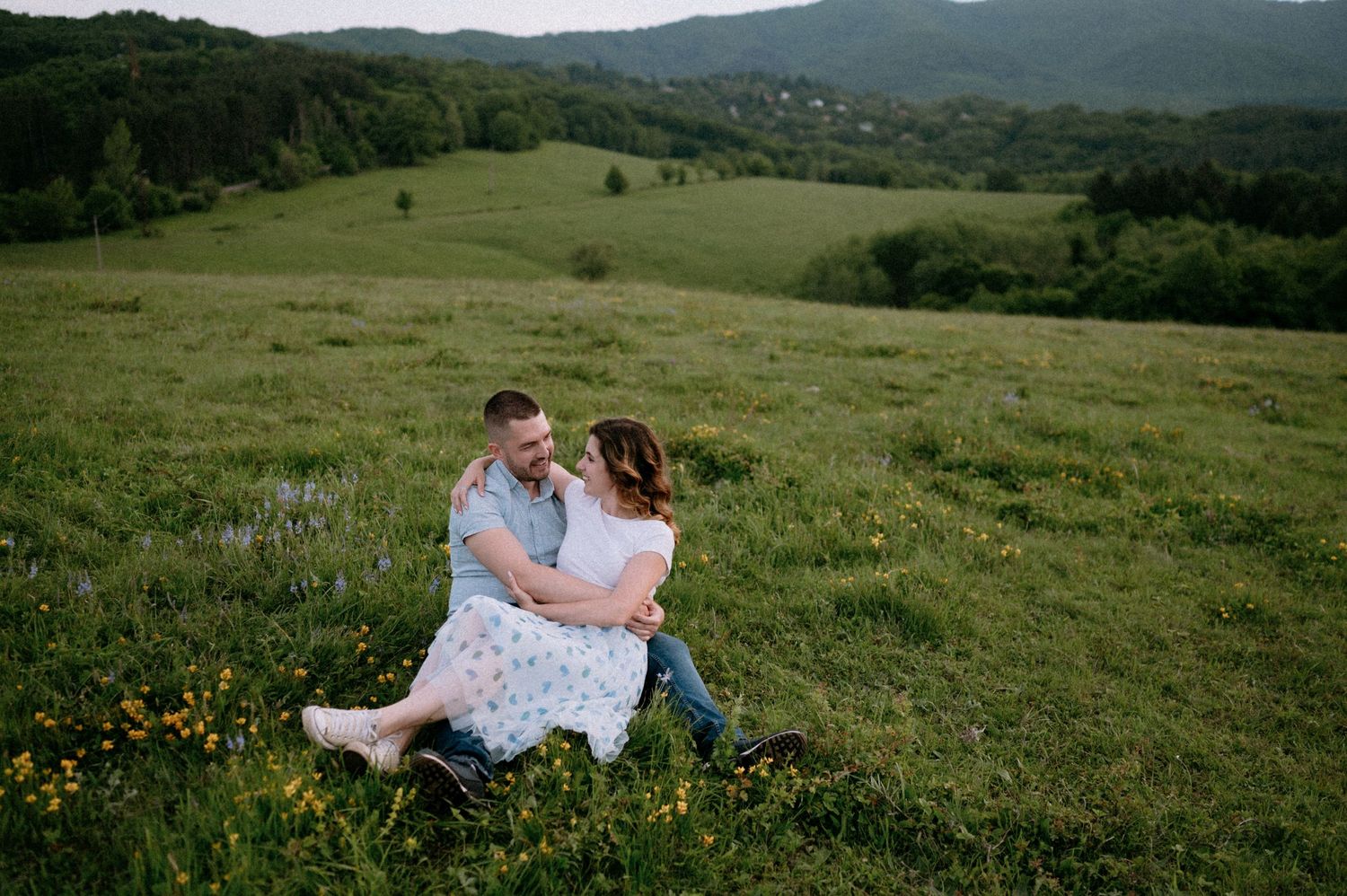 Two people share a tender moment while sitting in a mountain meadow with yellow wildflowers.