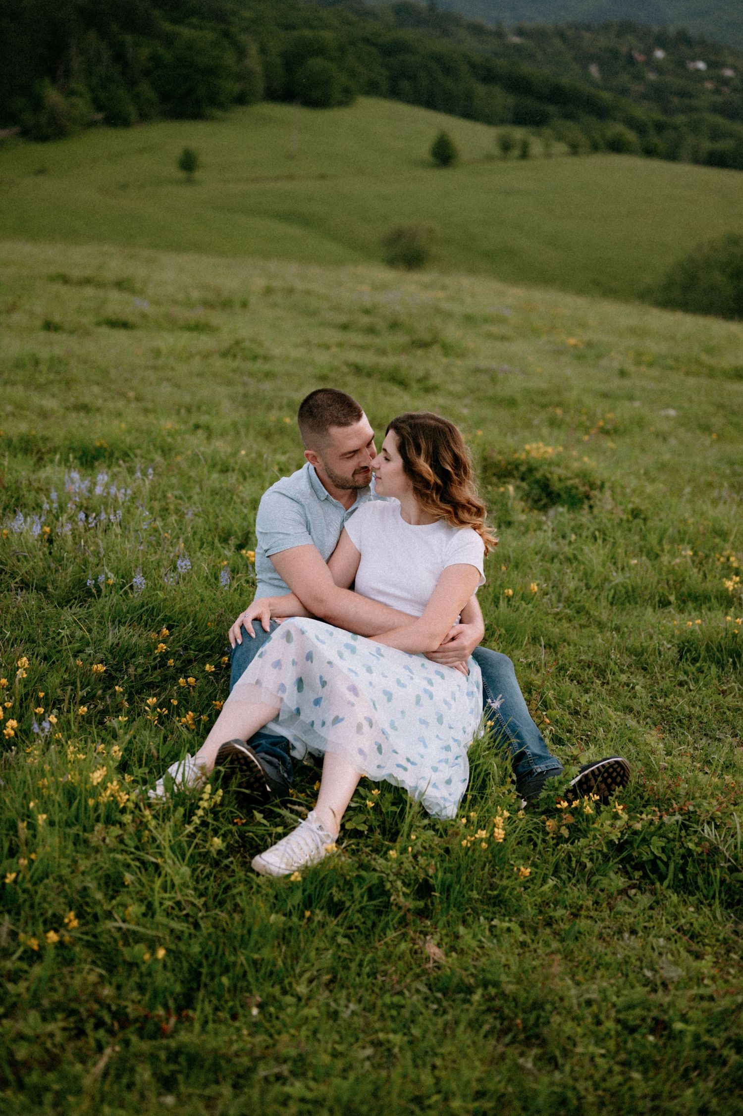 Couple shares intimate moment while sitting in a wildflower meadow with mountain views.