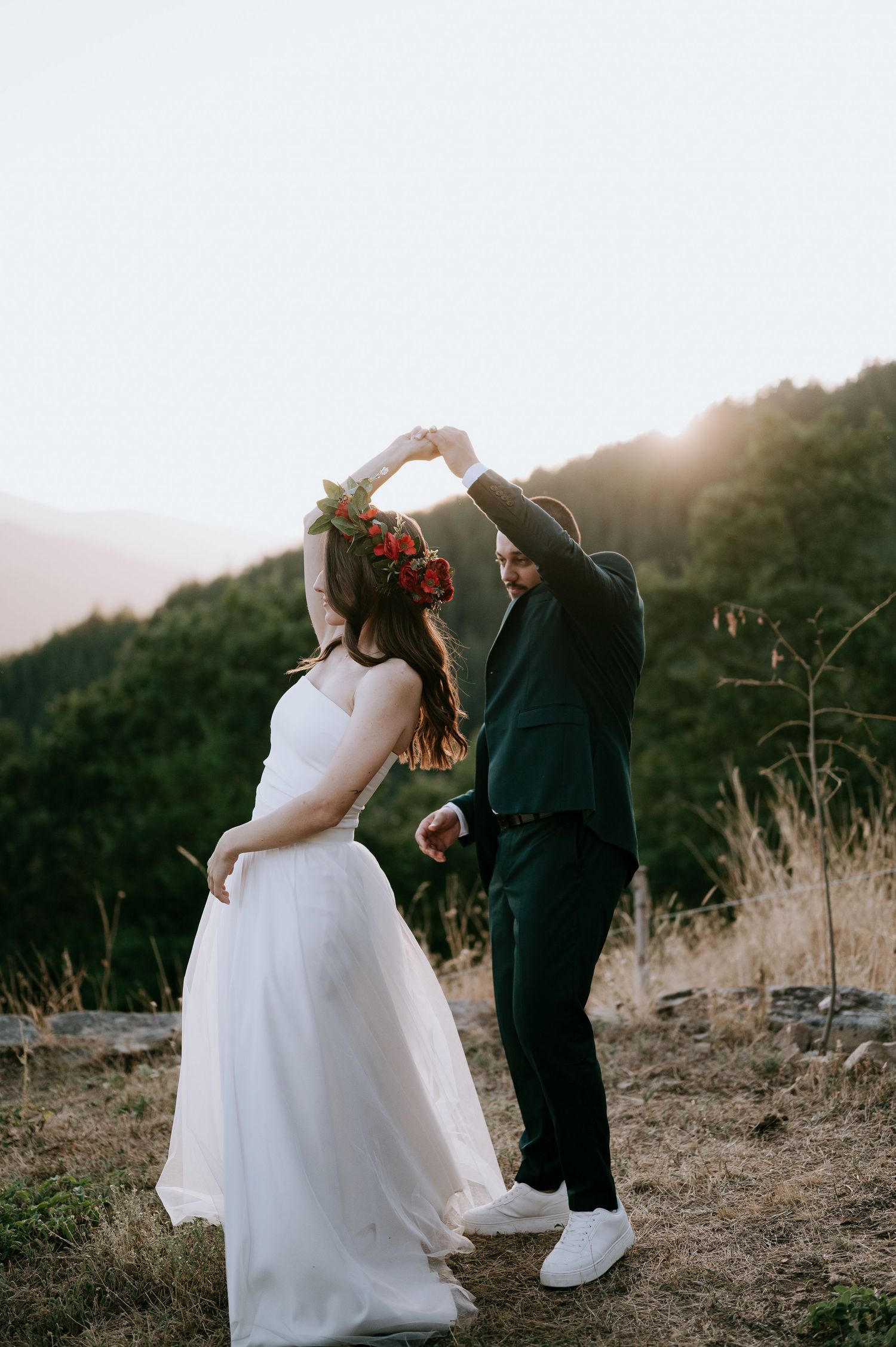 Newlyweds share a romantic dance pose against a mountain backdrop at sunset.
