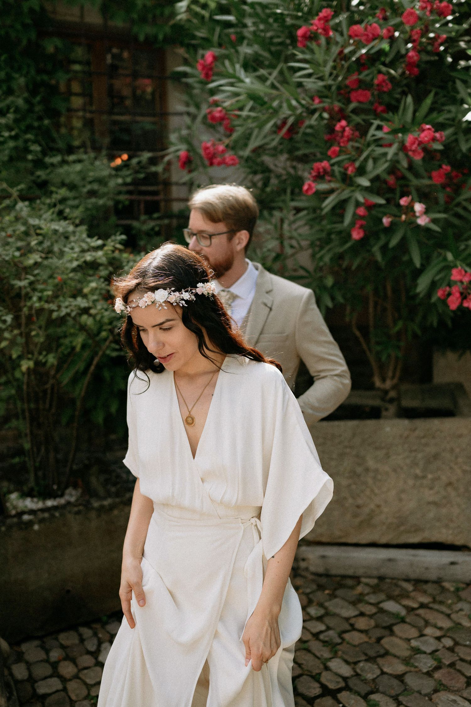 Couple in wedding attire dancing and twirling in a garden with red flowers.