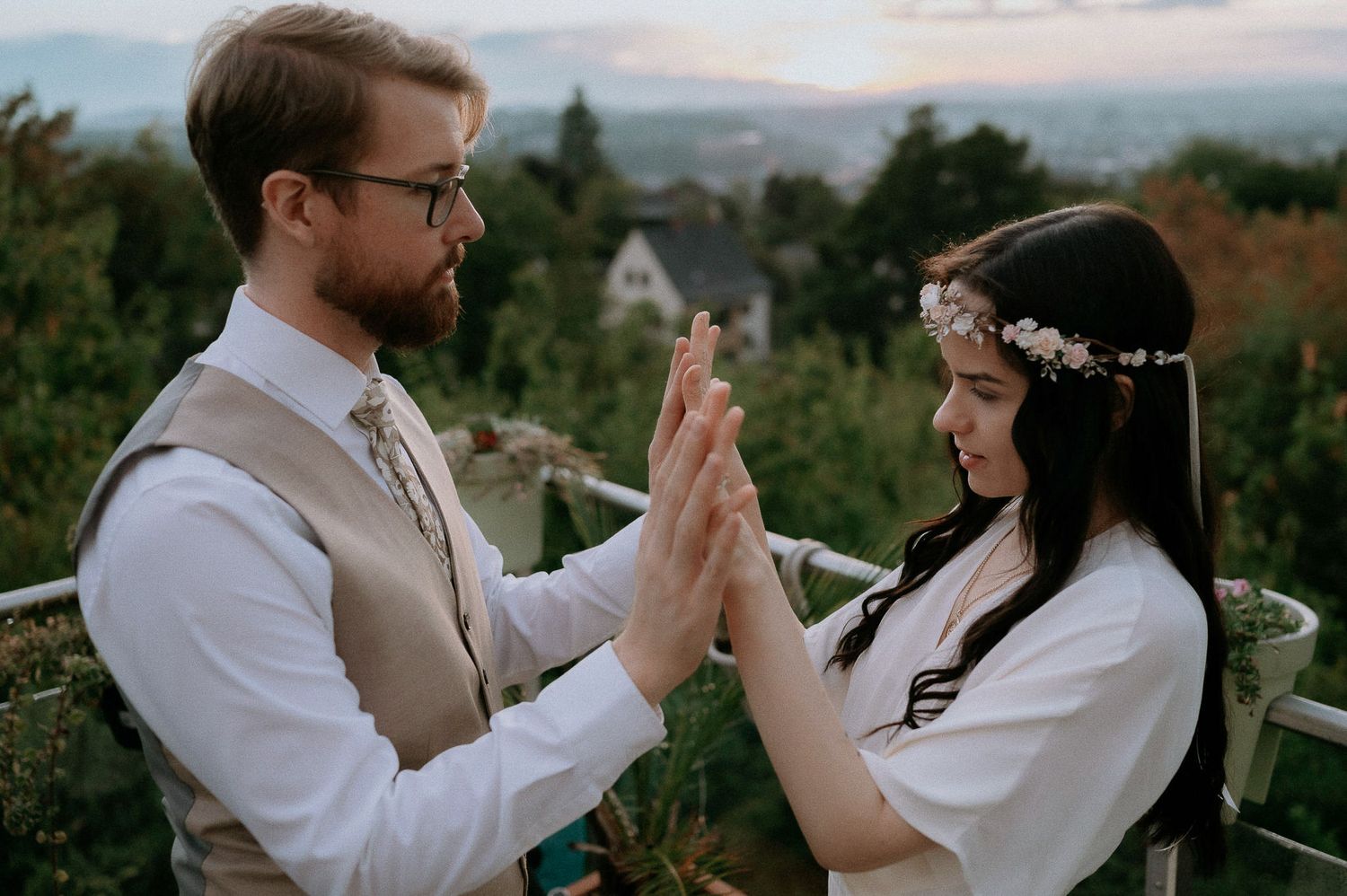 A couple in wedding attire giving each other a high five at sunset with mountains in the background.