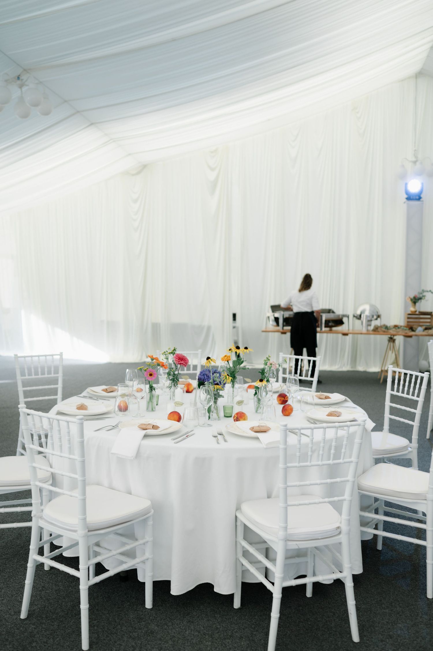 White wedding tent interior with round tables, chiavari chairs and draped fabric ceiling.