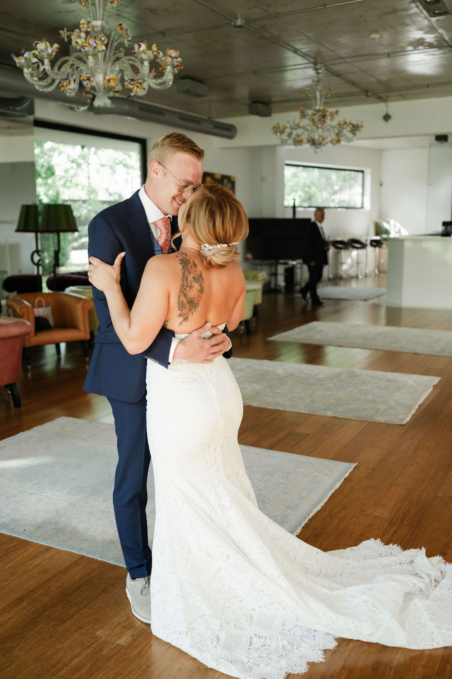 A tender embrace is shared during a wedding first look beneath an elegant chandelier.