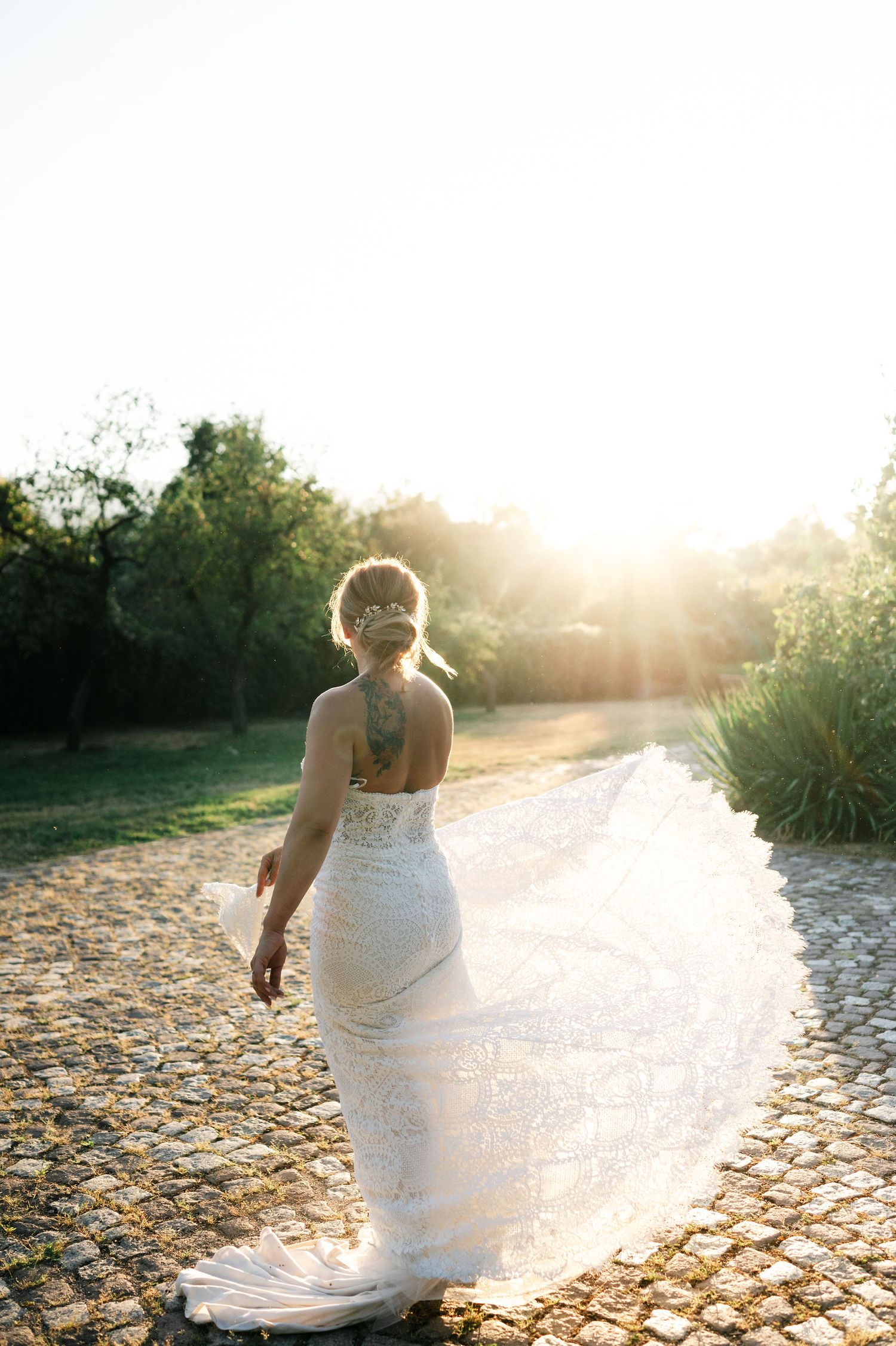 Wedding dress creates elegant silhouette against setting sun on textured stone pathway.