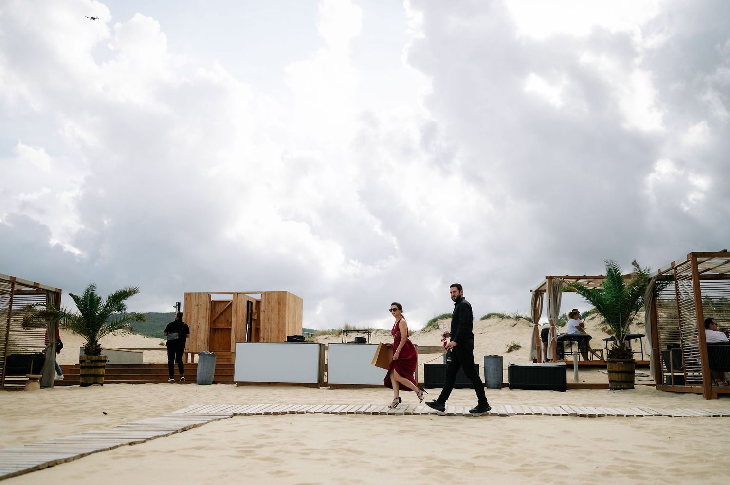 Panoramic view of a beach wedding setup with wooden structures and palm trees.